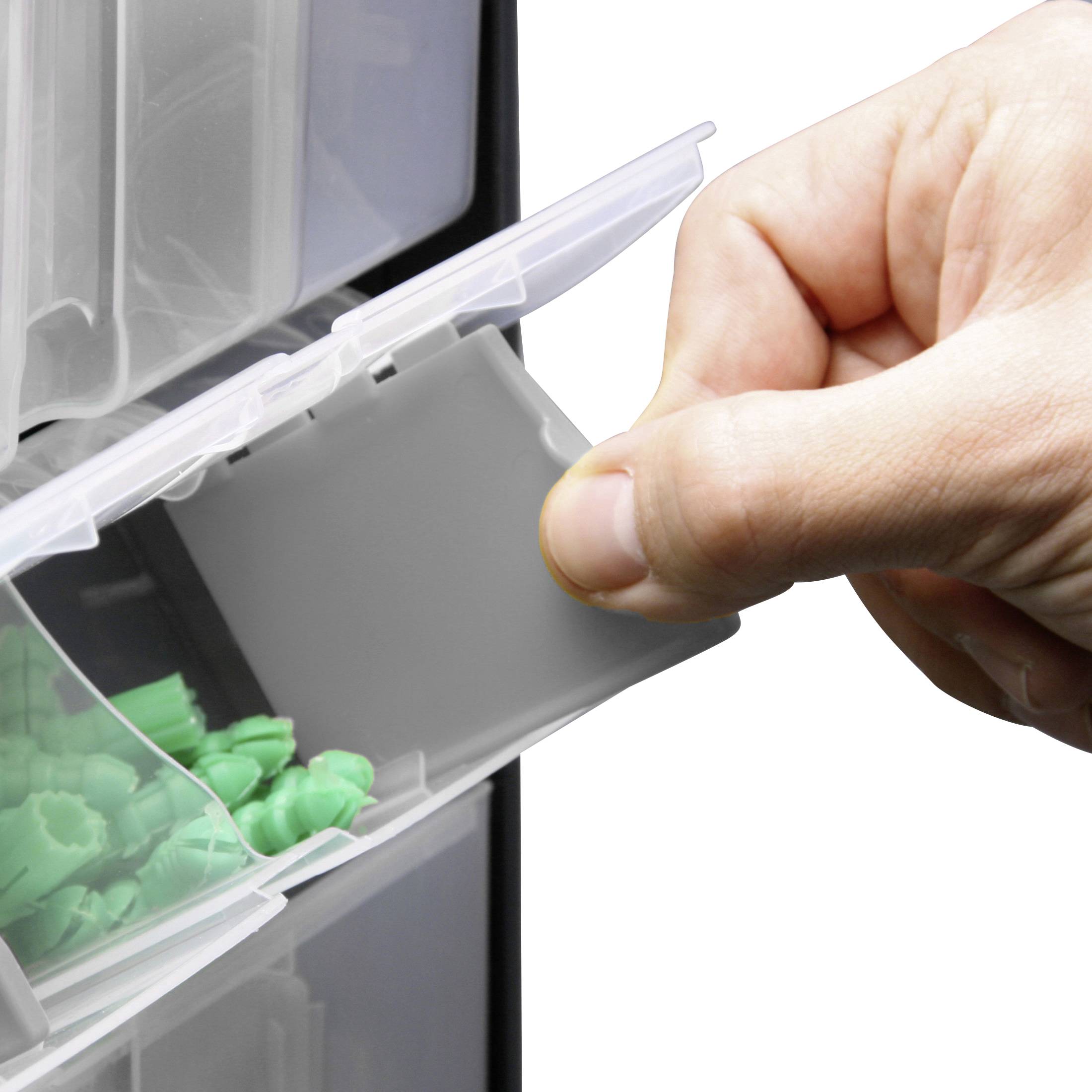 Dłoń otwiera małą plastikową przegródkę w systemie szufladowym, wypełnioną zielonymi plastikowymi elementami do gry.