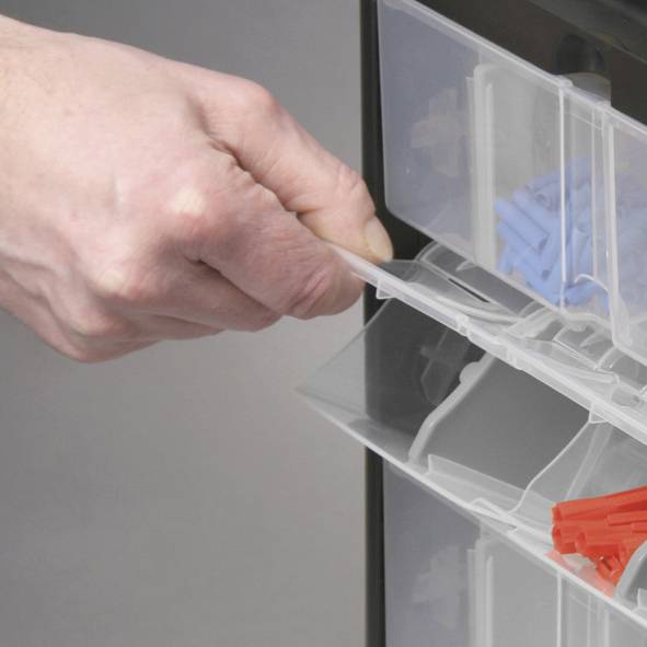 Dłoń wyciąga przezroczystą szufladkę z pudełka organizacyjnego. Szufladka zawiera niebieskie i czerwone plastikowe spinacze.