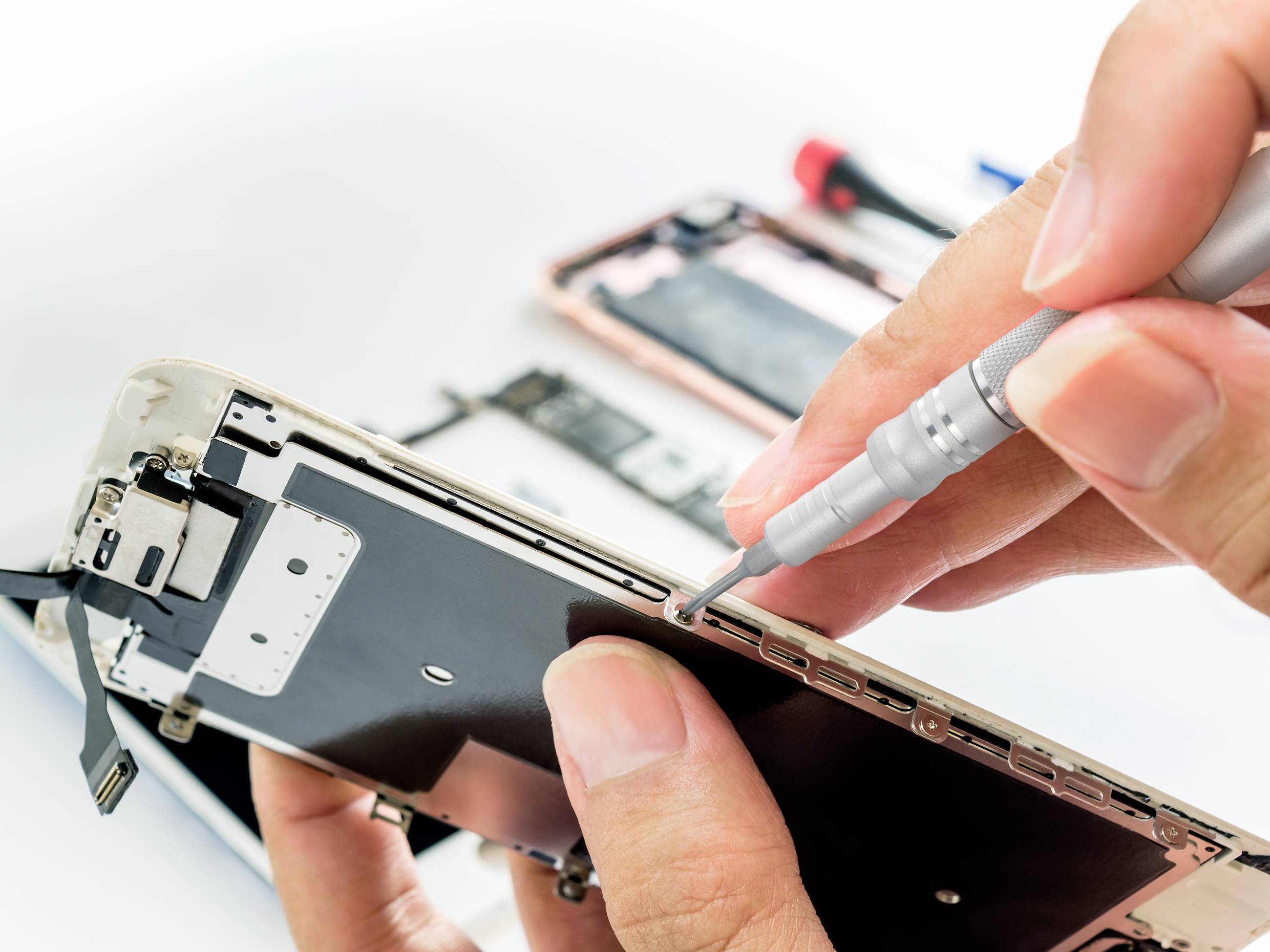 Zbliżenie przedstawia osobę naprawiającą smartfon wkrętakiem. Na pierwszym planie widać kilka narzędzi w tle.