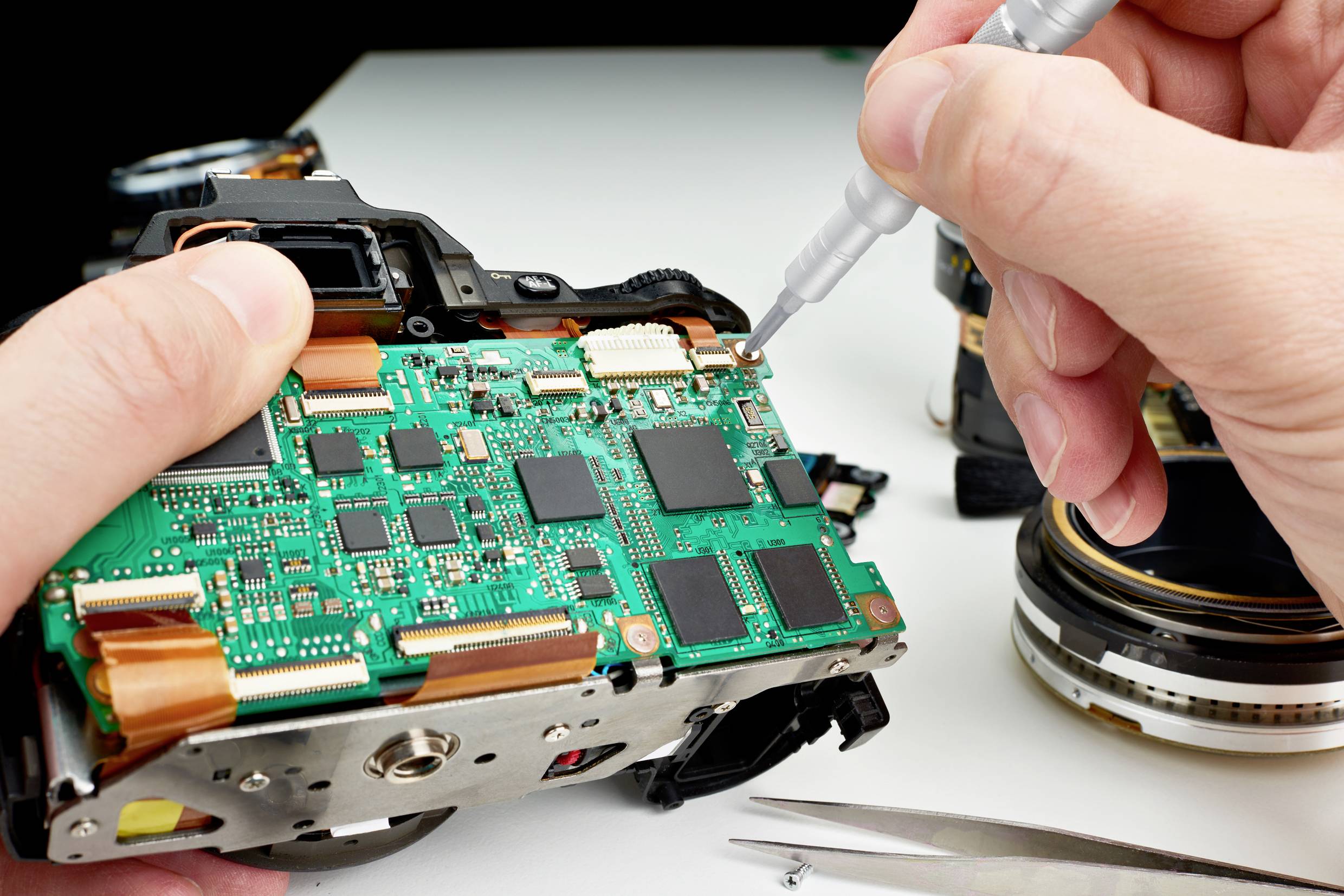 Inżynier elektronik naprawia kamerę, pracując narzędziem przy głównej płytce drukowanej.