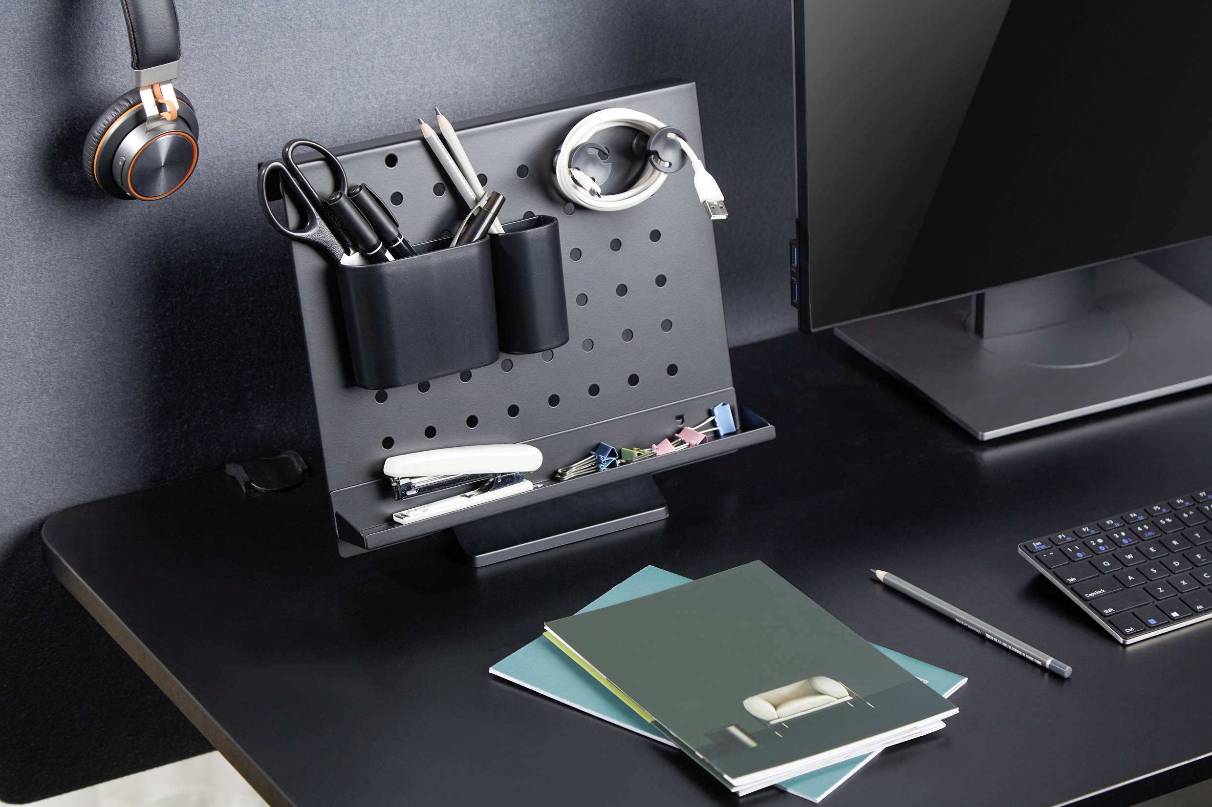 Biurko z przemyślanym systemem organizacji: nożyczki, długopis i słuchawki, obok ekranu komputera oraz zeszytów.