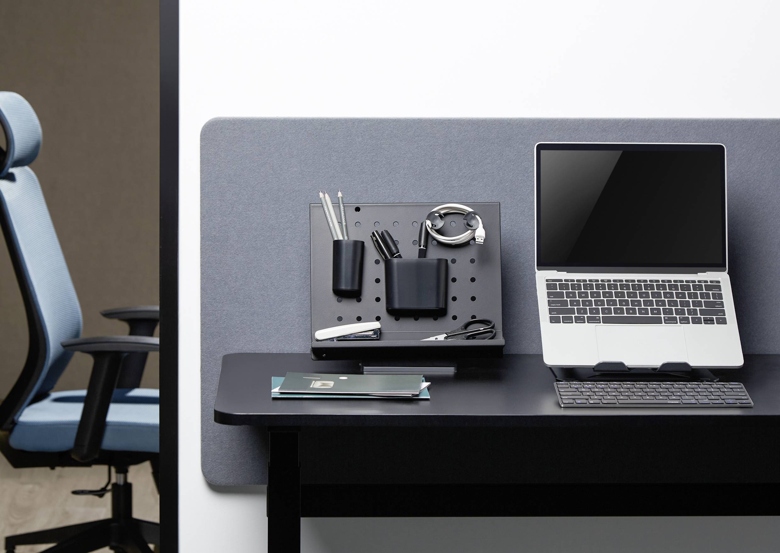 Laptop stoi na biurku obok artykułów biurowych i organizera.Bok niego znajduje się nowoczesny fotel biurowy.