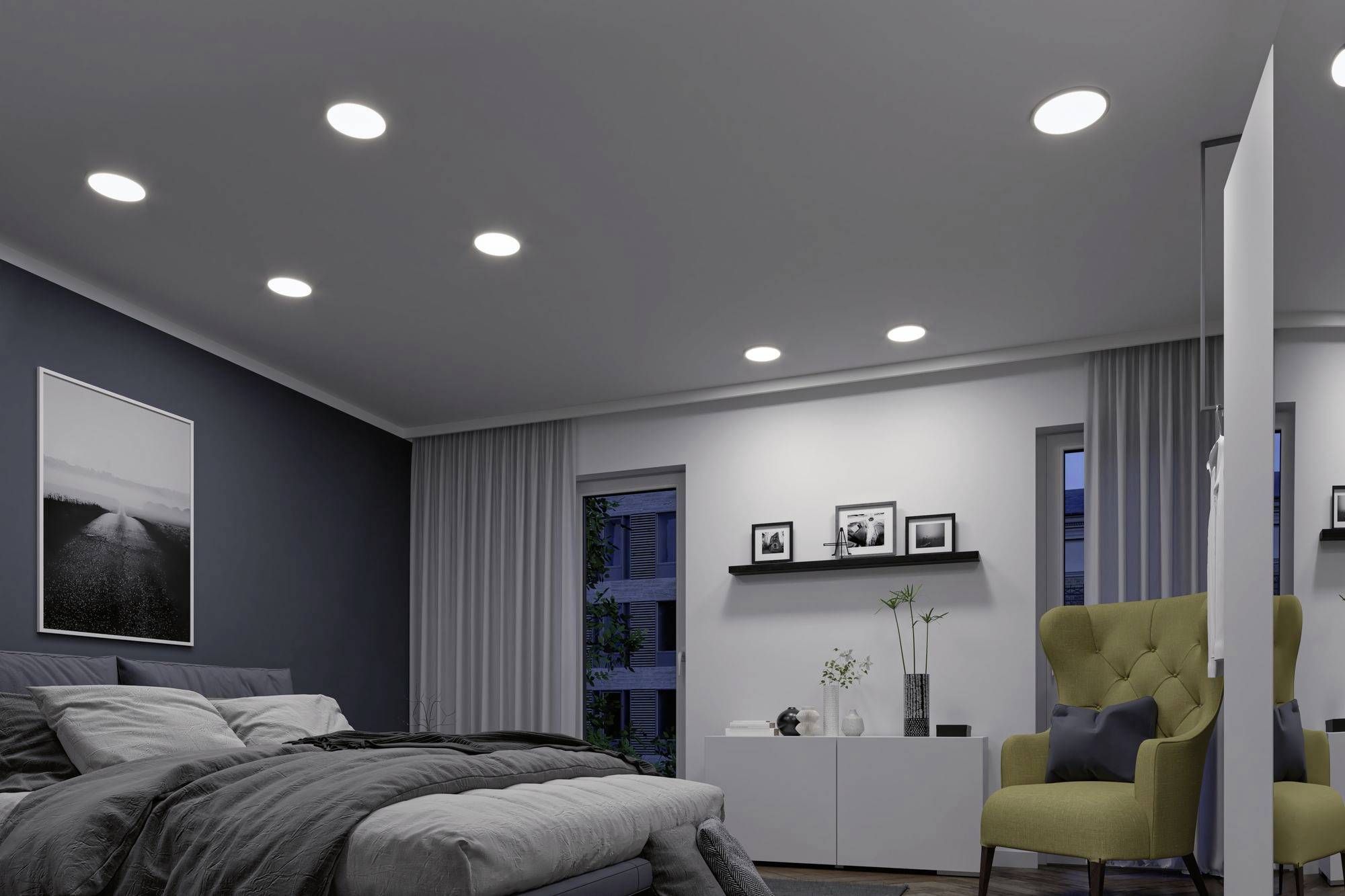 Sypialnia z nowoczesnymi lampami sufitowymi wpuszczanymi w sufit, szarym łóżkiem, żółtym fotelem oraz czarno-białymi zdjęciami na ścianie.