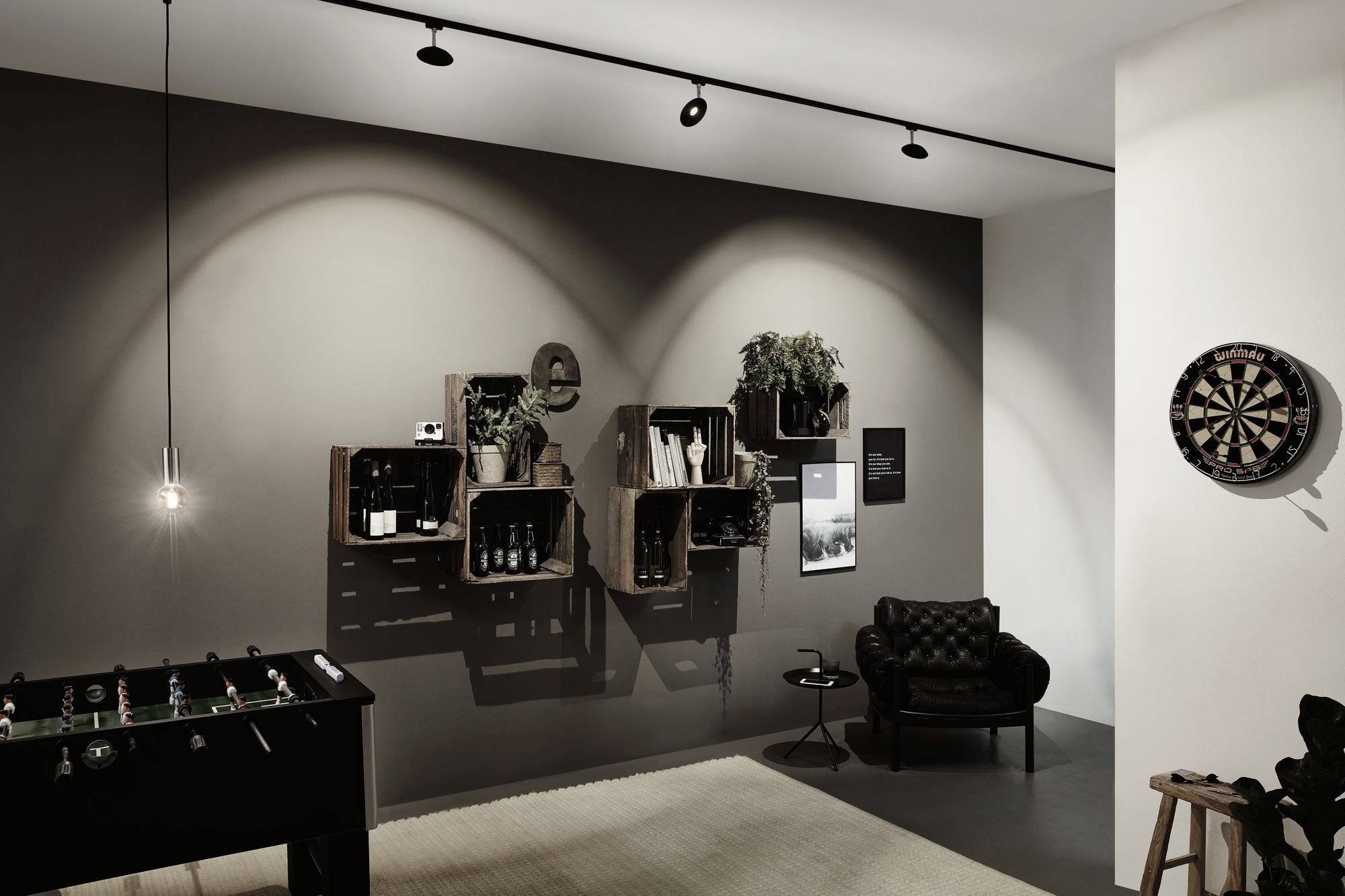 Stylowo urządzony salon z ciemną ścianą i pudełkami na regałach. Po lewej stronie stoi piłkarzyki, po prawej wisi tarcza do darta.