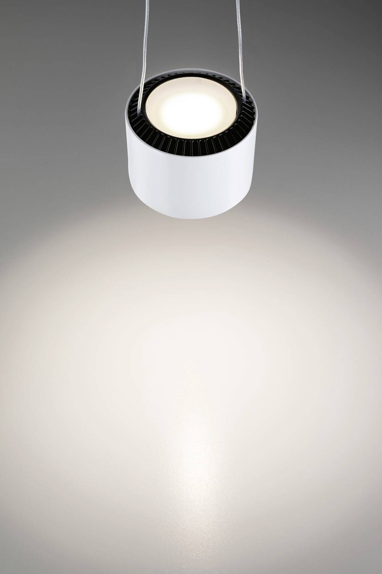 Lampa wisząca z okrągłym, białym kloszem, świecąca w dół i tworząca okrągły wzór świetlny na szarym tle.