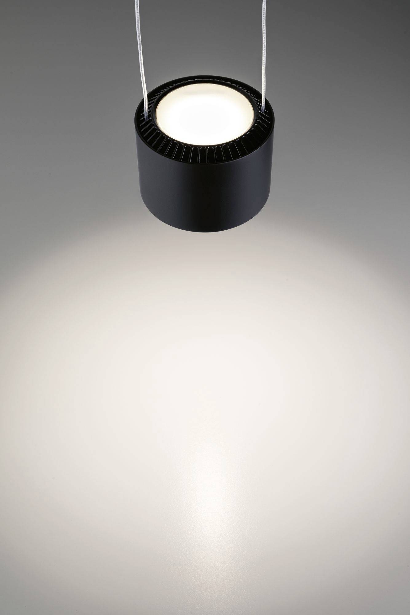 Pojedyncza, nowoczesna lampa sufitowa zwisa z sufitu i rzuca jasne światło na gładką, szarą powierzchnię poniżej.