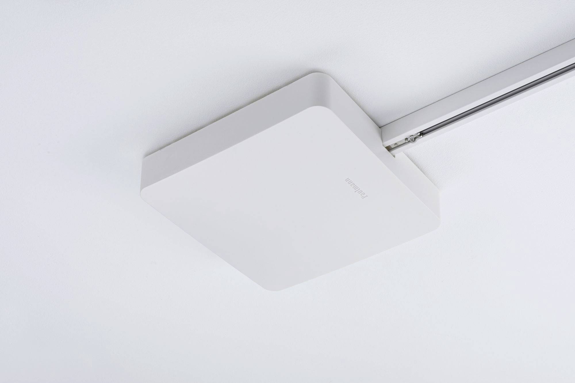 Biały, kwadratowy głośnik sufitowy jest zamontowany na szynie aluminiowej przymocowanej do sufitu.