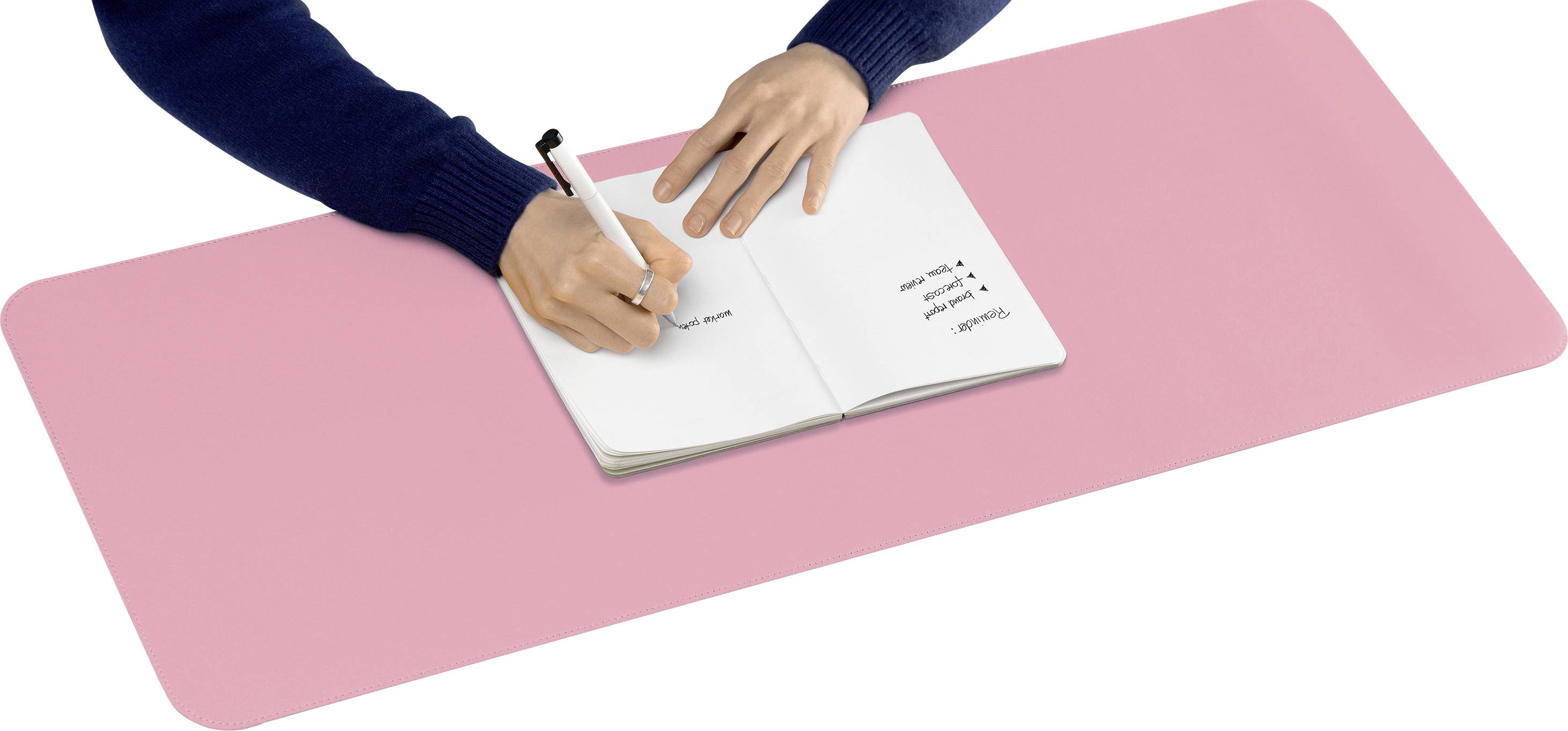 Osoba pisze długopisem w zeszycie na dużej różowej podkładce biurkowej.
