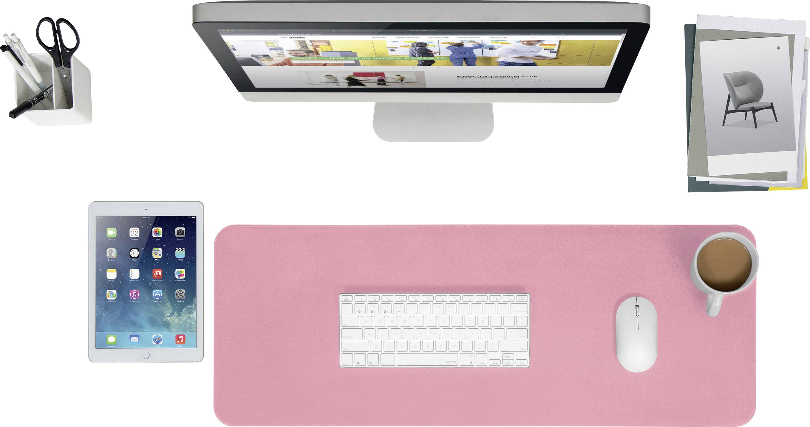 Biurko z monitorem, klawiaturą i myszą na różowej macie, obok tablet, pojemnik na długopisy i filiżanka kawy. W tle leżą niektóre broszury.