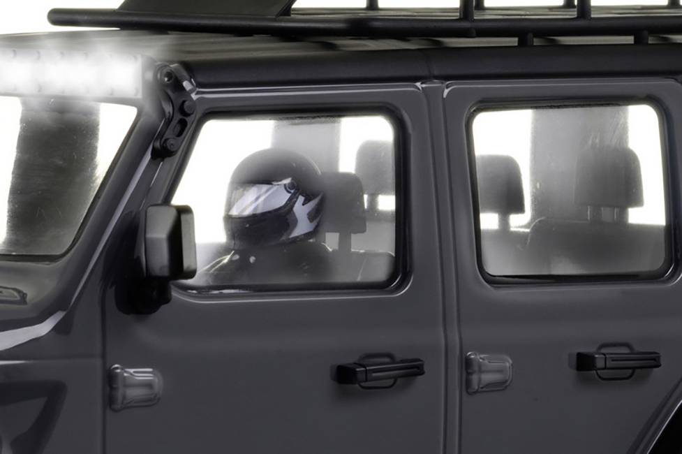 Osoba siedząca w samochodzie patrzy przez okno. Pojazd jest szary i wygląda na solidny, prawdopodobnie przystosowany do jazdy w trudnym terenie.