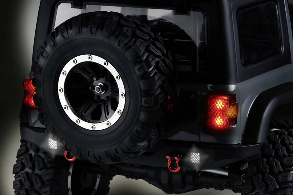 Terenówka z dużymi oponami i dwoma czerwonymi hakami z tyłu. Tylne światła są włączone. Samochód wydaje się być gotowy do przygód terenowych.