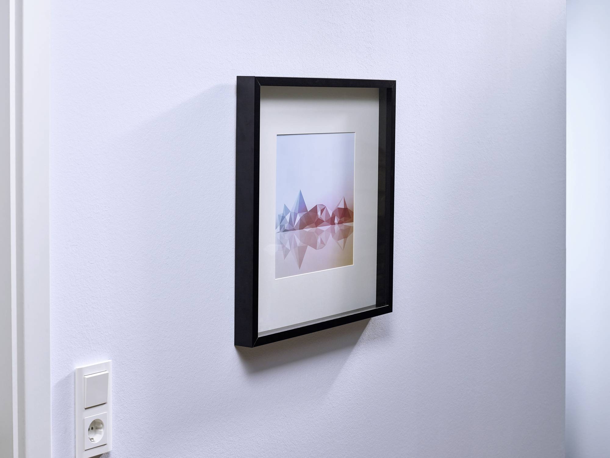 Oprawione dzieło sztuki na białej ścianie. Abstrakcyjne geometryczne formy w odcieniach błękitu i czerwieni. Przełącznik widoczny w lewym dolnym rogu.