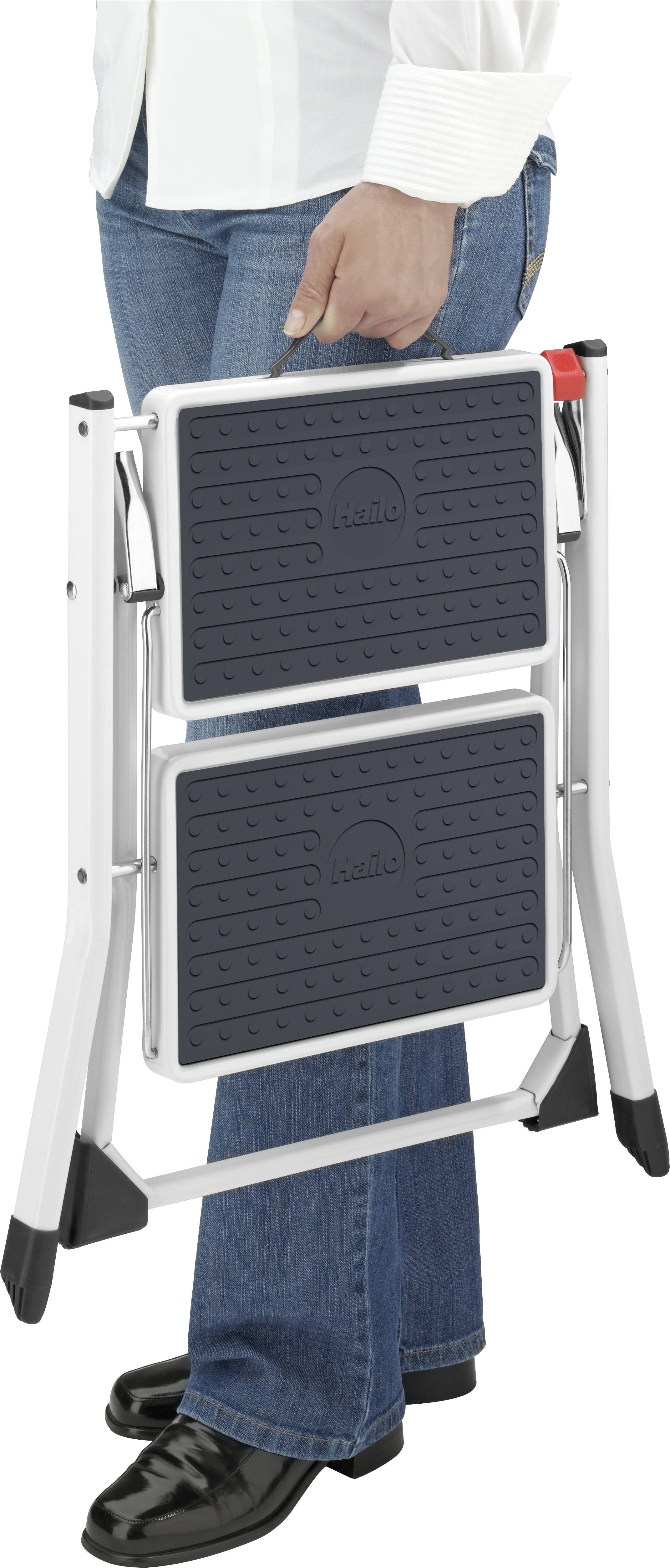 Osoba trzyma złożony taboret składany w ręku. Stołek jest czarno-srebrny, z antypoślizgowymi stopniami.