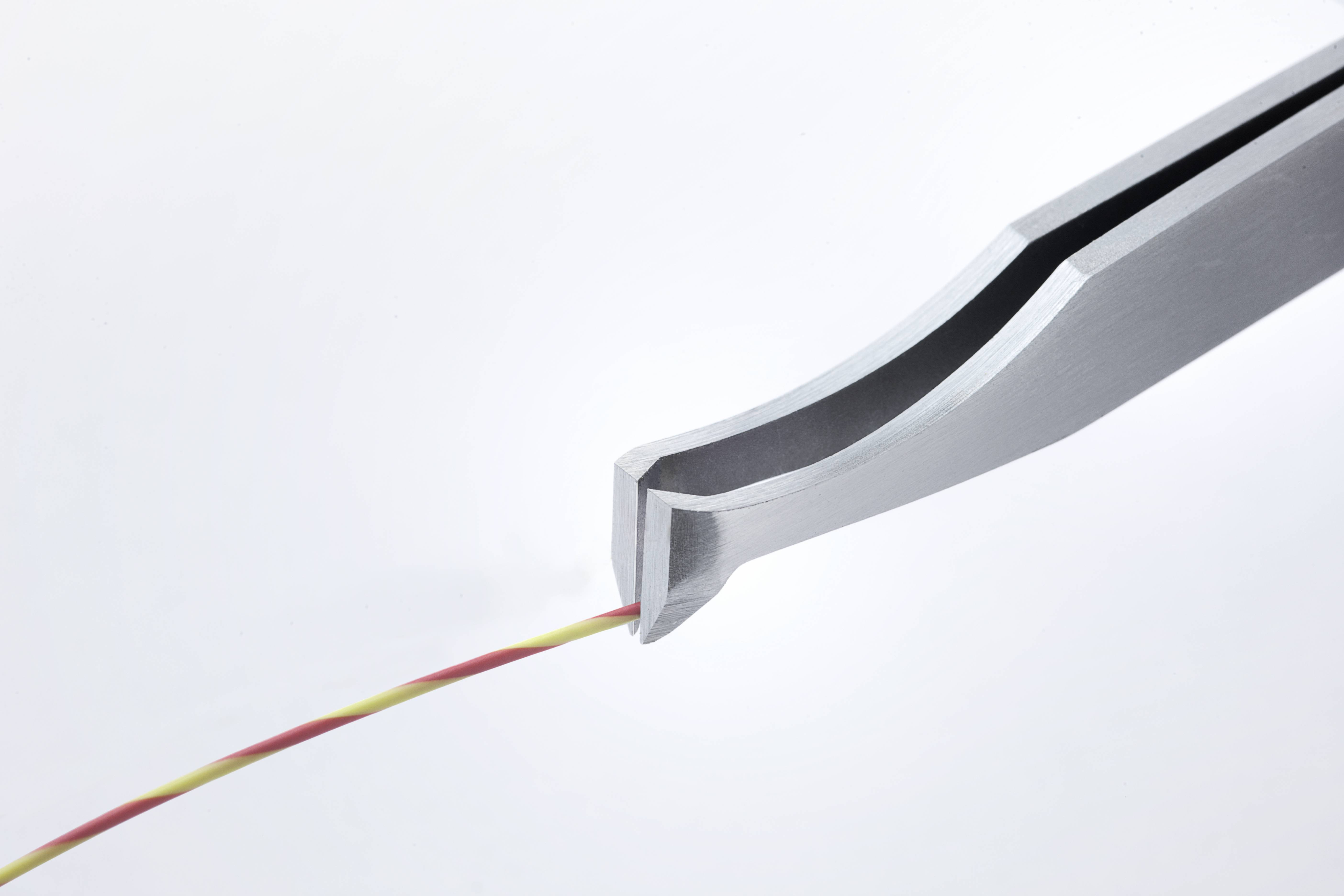 Drut jest trzymany przez szczypce. Drut jest dwukolorowy, czerwony i żółty. Szczypce mają metalową powierzchnię.