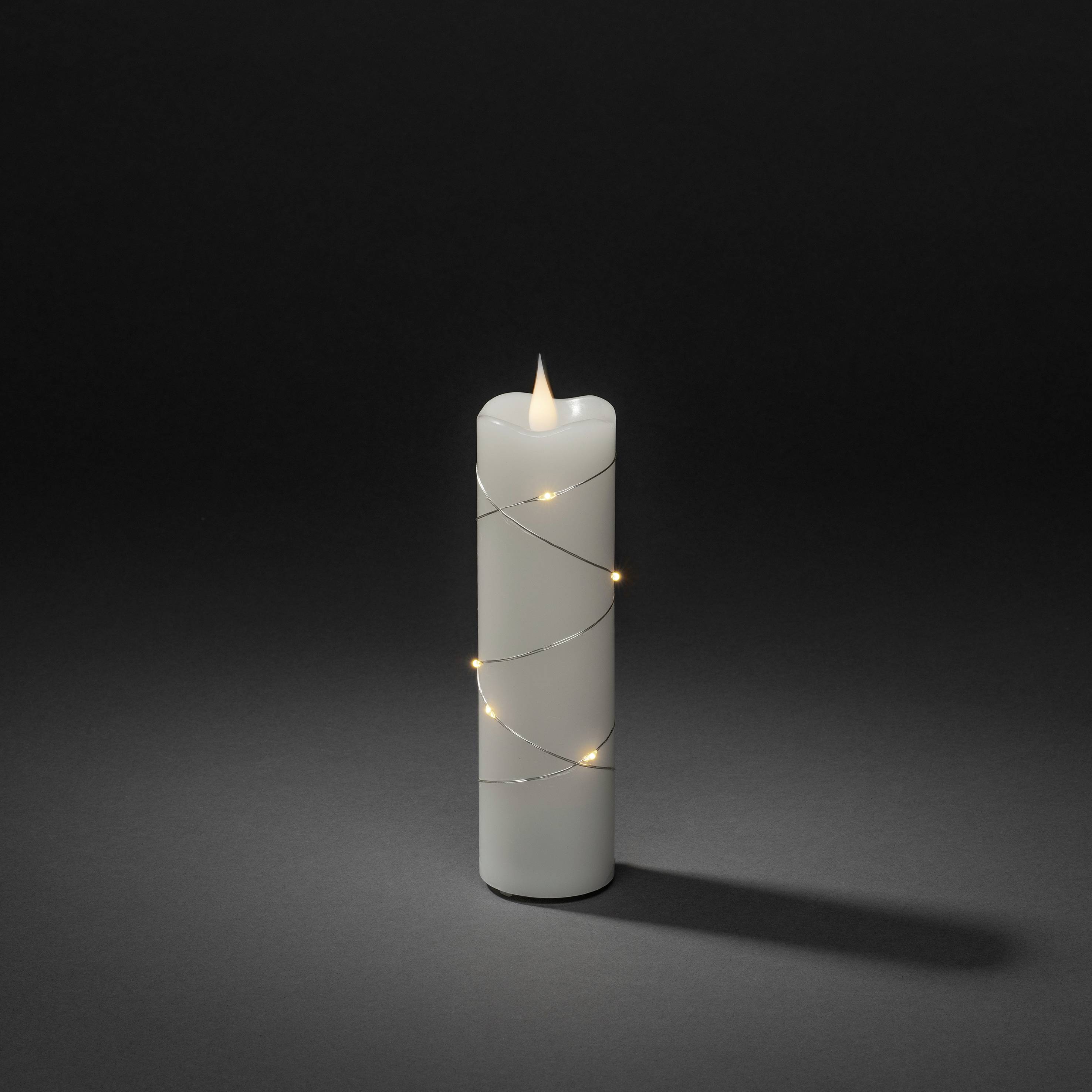 Biała świeca owinięta cienkim, świecącym drutem stoi na ciemnym tle.