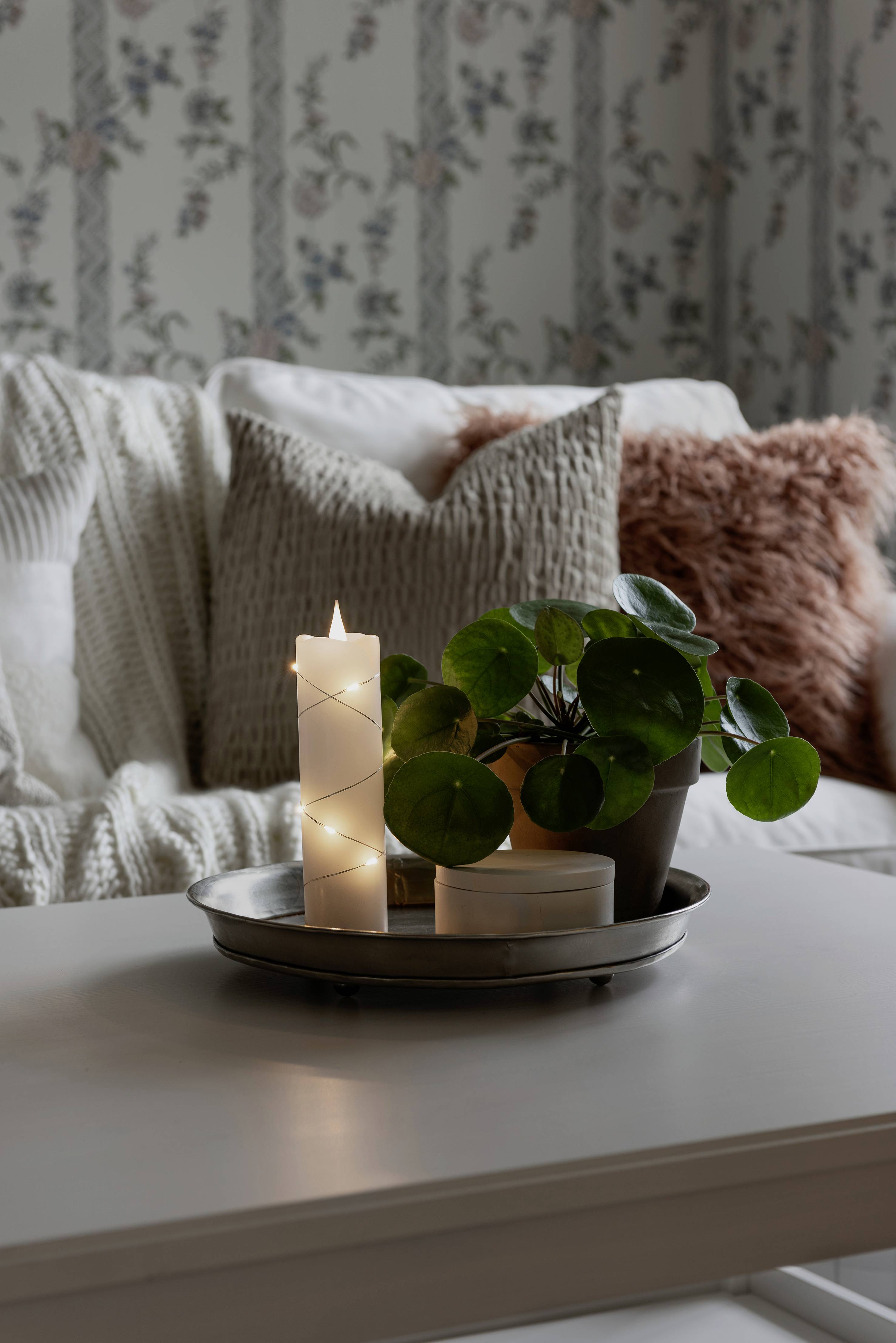 Świece i roślina na stole, w tle przytulna sofa z poduszkami. Przytulna i zapraszająca atmosfera salonu.