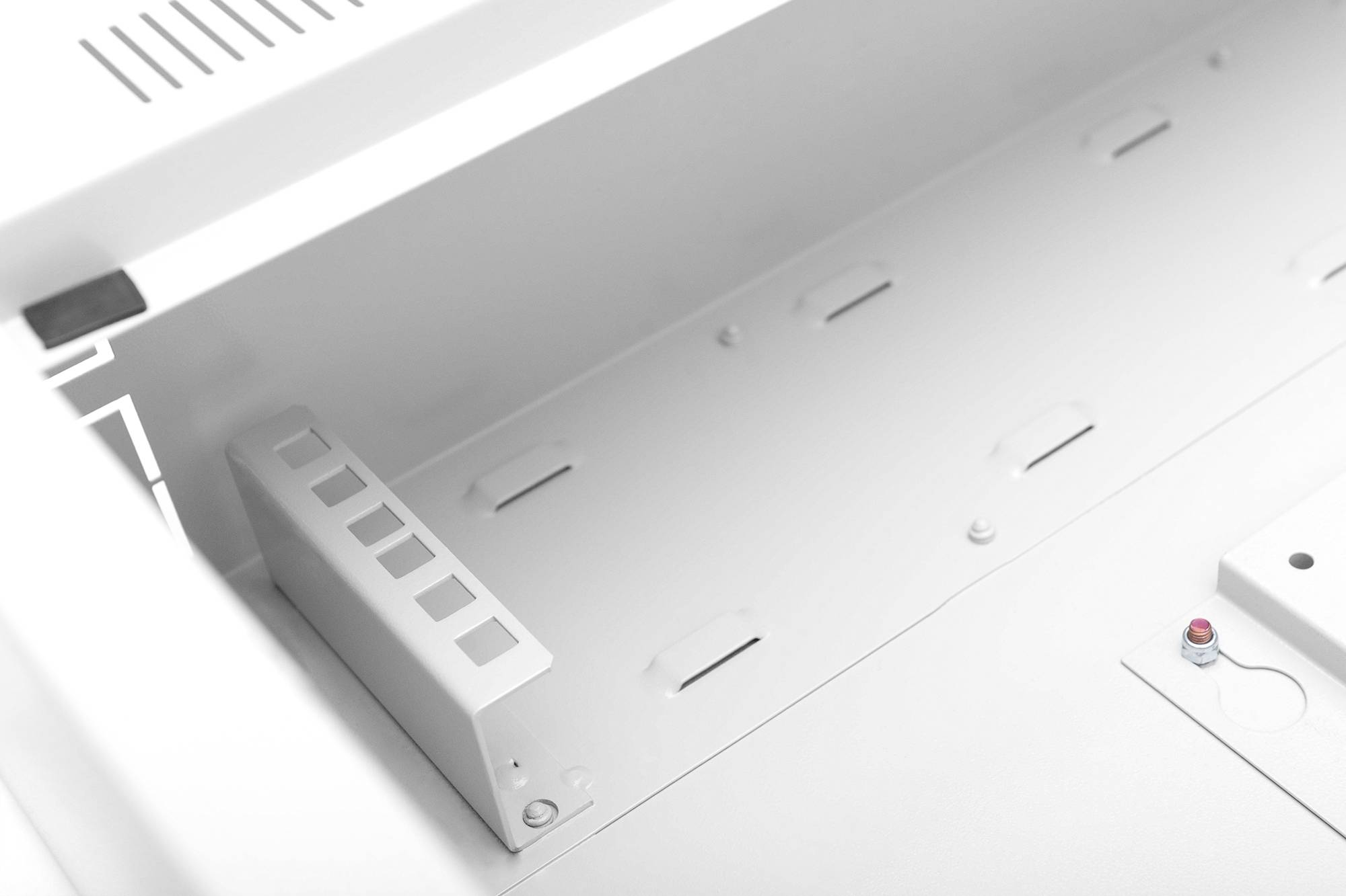 Pusty, biały wewnętrzny obszar szafki z kilkoma otworami wentylacyjnymi i małym czerwonym przyciskiem w prawym dolnym rogu.