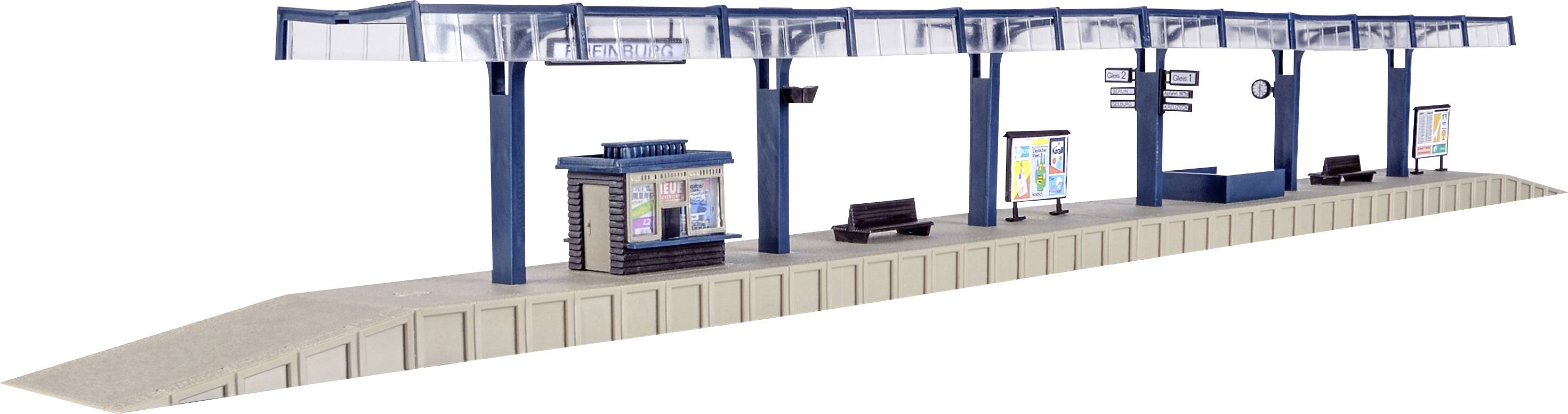 Mały peron modelarskiej kolejki z poczekalnia, ławkami i tablicami reklamowymi.