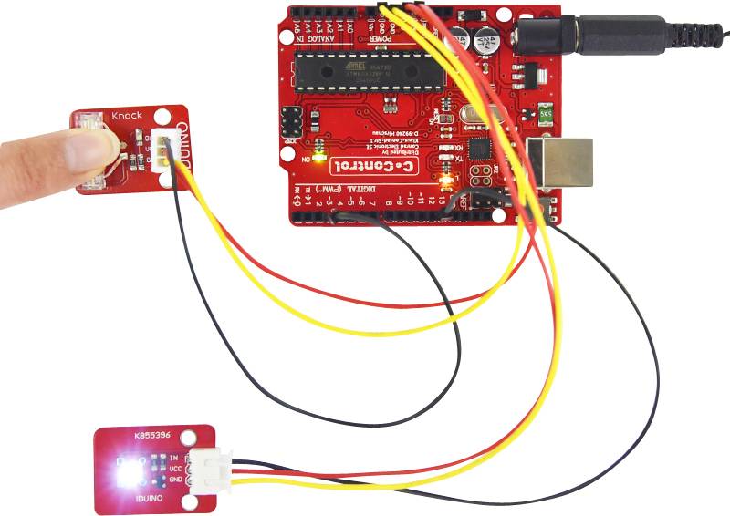 Czerwona płytka mikrokontroli jest podłączona do czujnika drgań i świecącego modułu LED. Ręka wskazuje na czujnik.