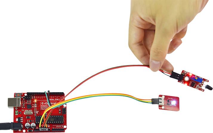 Ręka trzyma czujnik podłączony przewodami do czerwonego mikrokontrolera. Kolejny czujnik jest również podłączony.