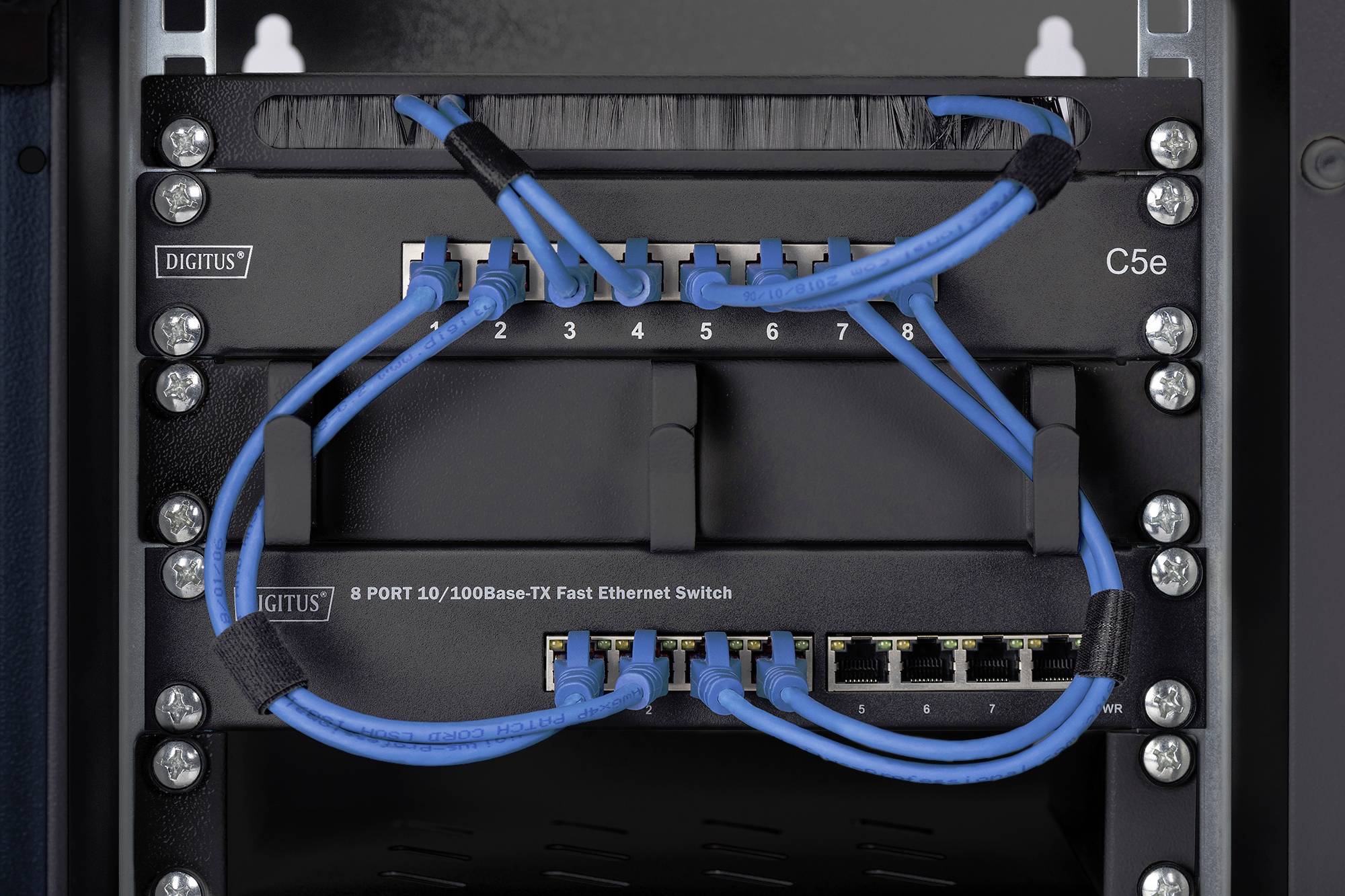 Przełącznik sieciowy z ośmioma niebieskimi kablami Ethernet włożonymi do portów. Opisany jako '8 PORT 10/100Base-TX Fast Ethernet Switch'.