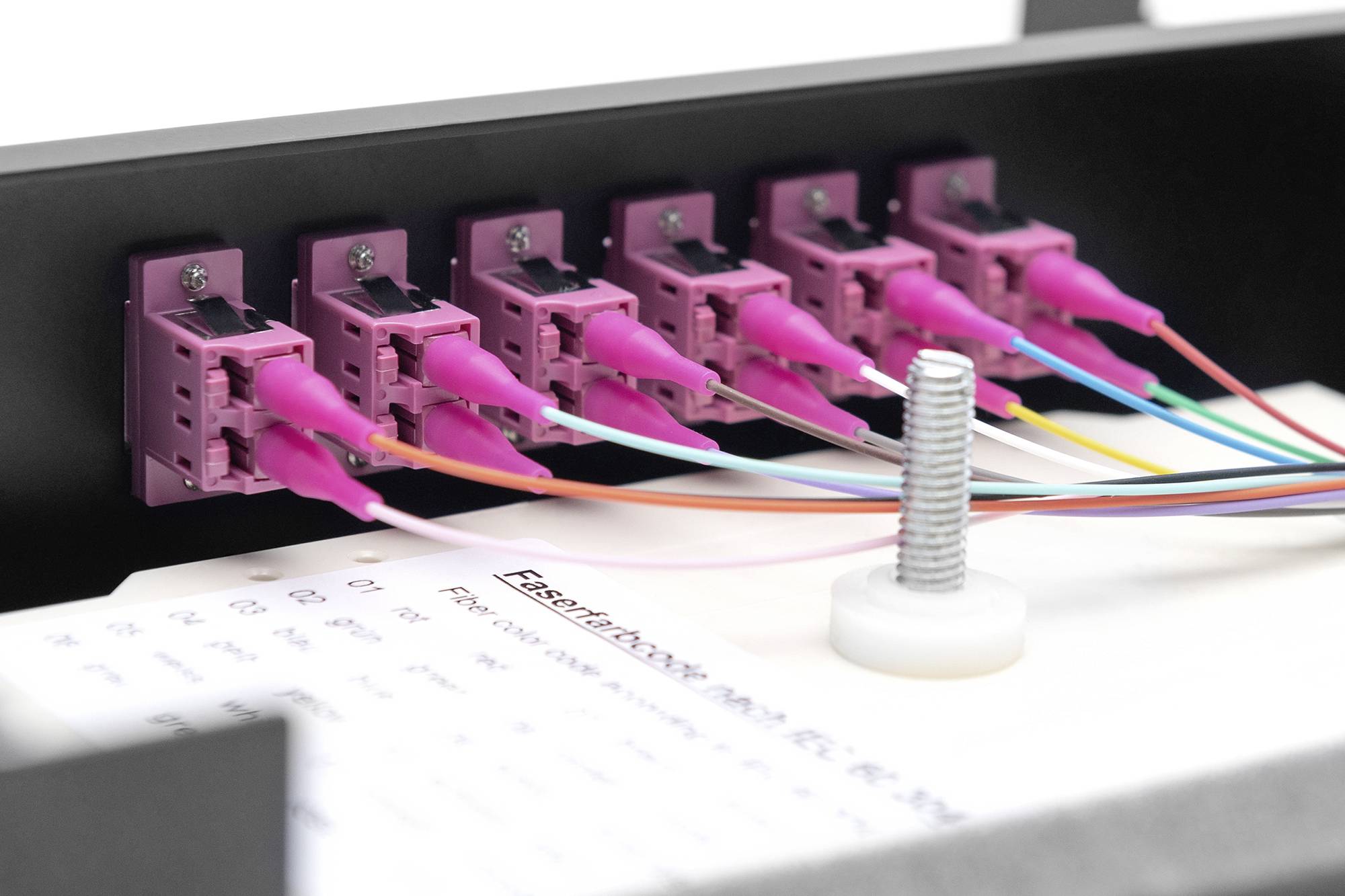 Kilka różowych złączy światłowodowych z podłączonymi kablami w urządzeniu sieciowym.