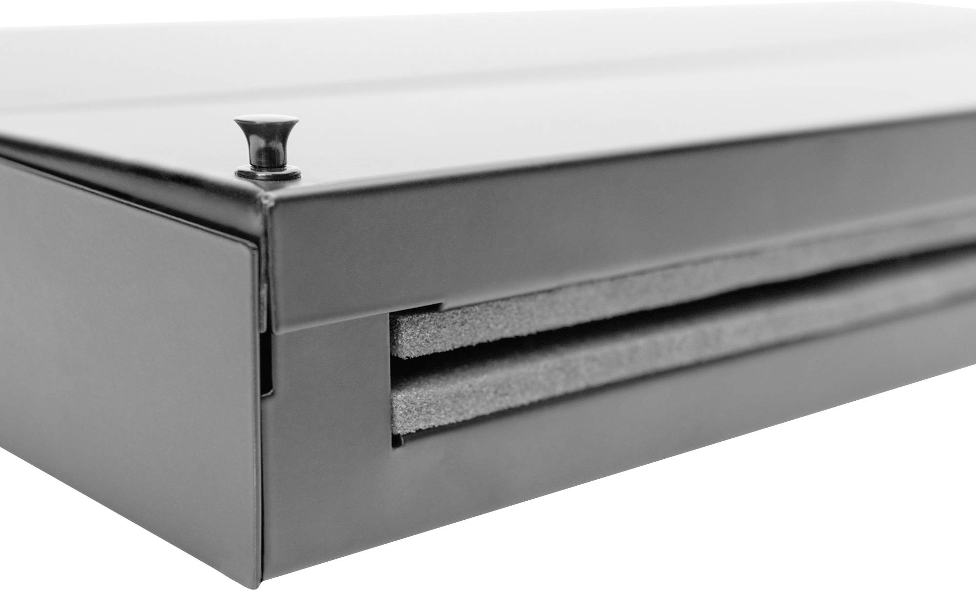 Zbliżenie zamkniętego czarnego pudełka wyłożonego wewnątrz warstwą pianki ochronnej. Mały metalowy guzik znajduje się na górnej powierzchni.