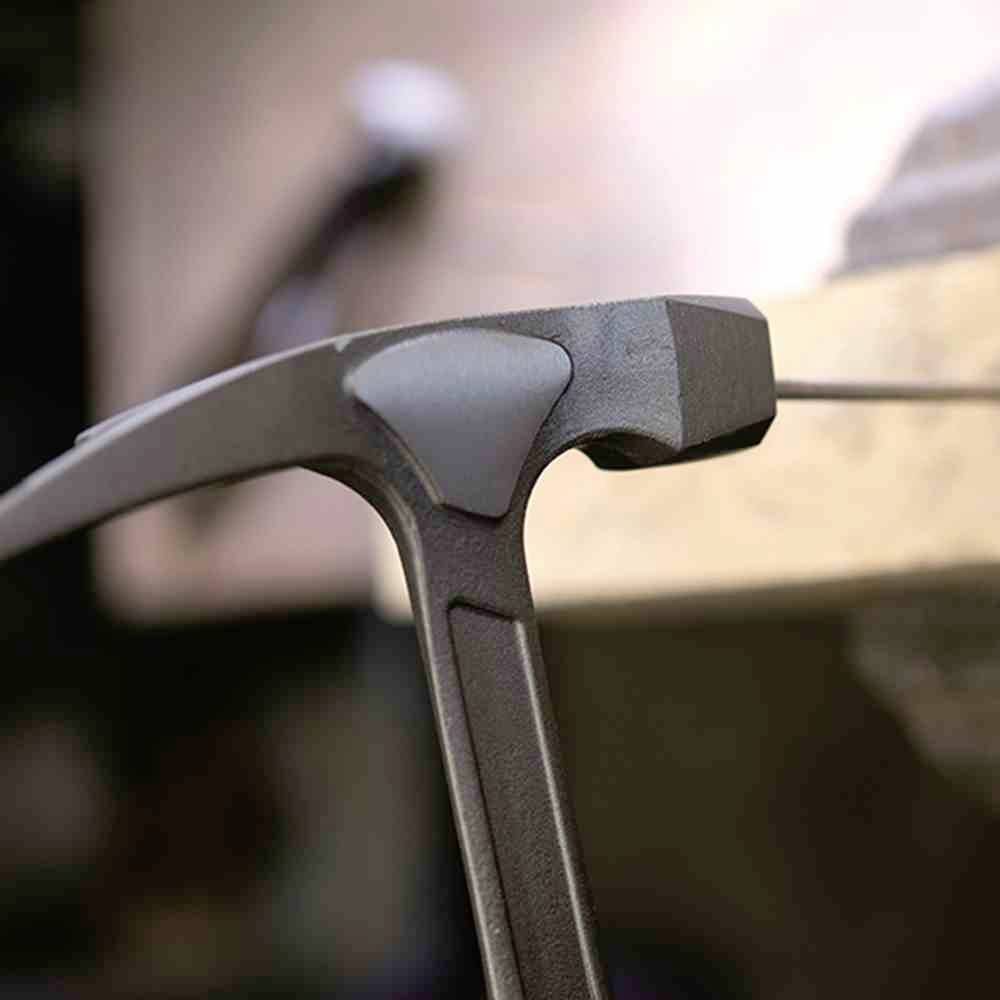 Ciemny metalowy młotek o prostokątnej główce i ergonomicznym uchwycie leży w pobliżu drewnianej powierzchni w warsztacie.