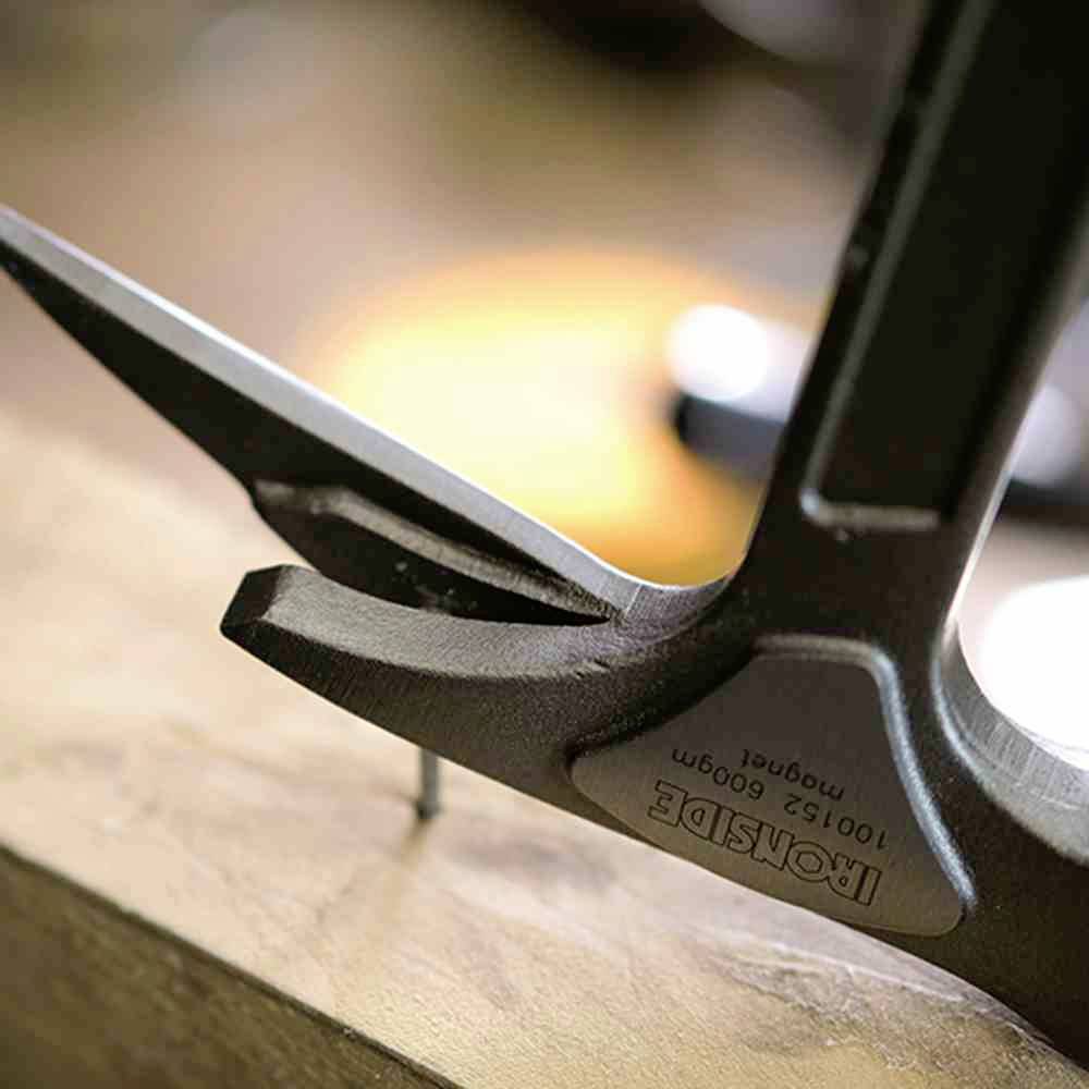 Czarny młotek wyciąga gwóźdź z deski drewnianej. Uchwytem skierowanym w lewo, wyróżniony gwóźdź jest już niemal wyrwany.