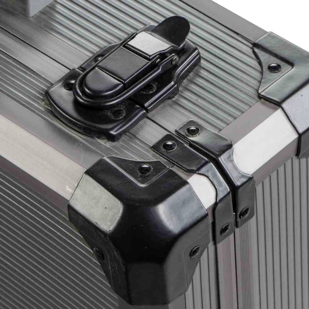 Metalowa skrzynka z czarnymi metalowymi narożnikami i czarną klamrą zamykającą na górze, stojąca na powierzchni z wypukłościami.