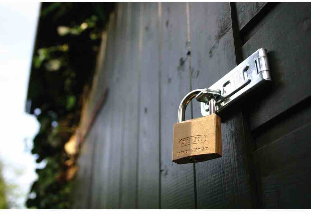 Kłódka zabezpiecza drewnianą deskę na ciemnej ścianie. Symbolizuje bezpieczeństwo lub ochronę.