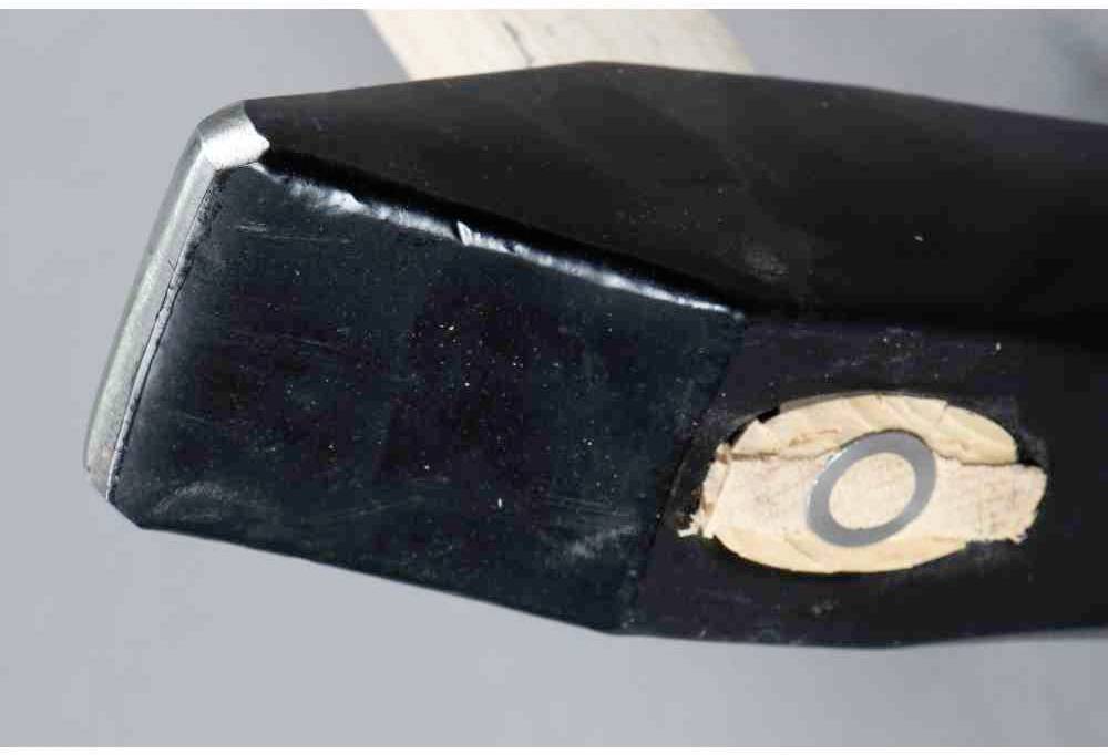 Czarny młotek z metalową głowicą i drewnianym uchwytem. Młotek jest lekko pochylony na bok, na szarym tle.