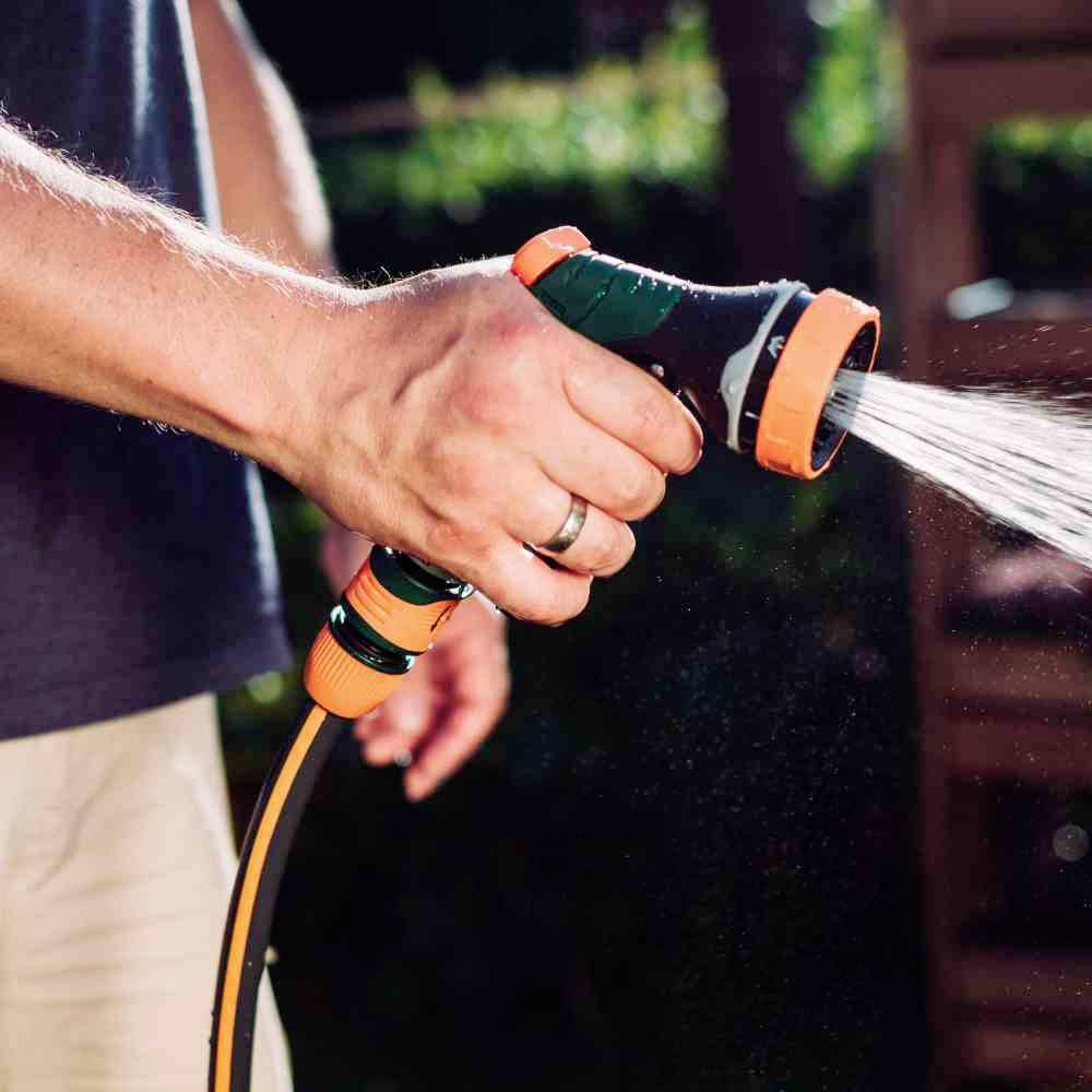 Osoba trzyma wąż ogrodowy z natryskiem, z którego tryska woda, podczas pracy w ogrodzie.