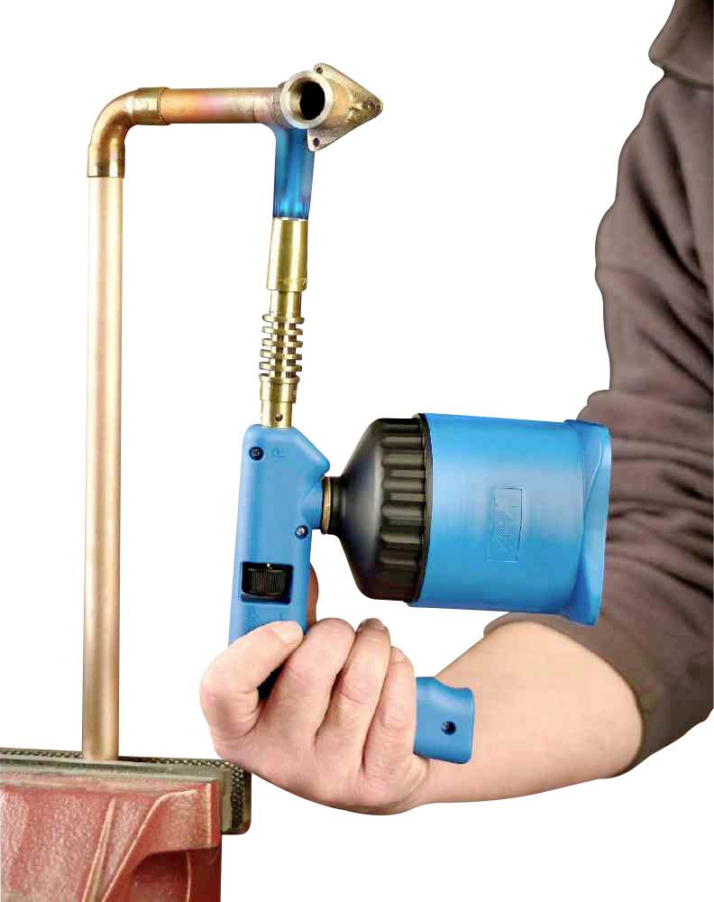 Osoba używa niebieskiego narzędzia do podgrzewania rury miedzianej w imadle.