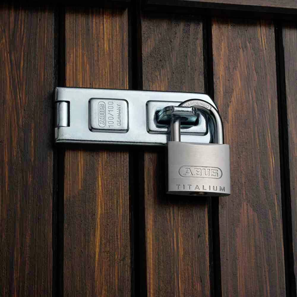 Srebrna kłódka z napisem 'Abus Titalium' zabezpiecza zamkniętą drewnianą barykadę.