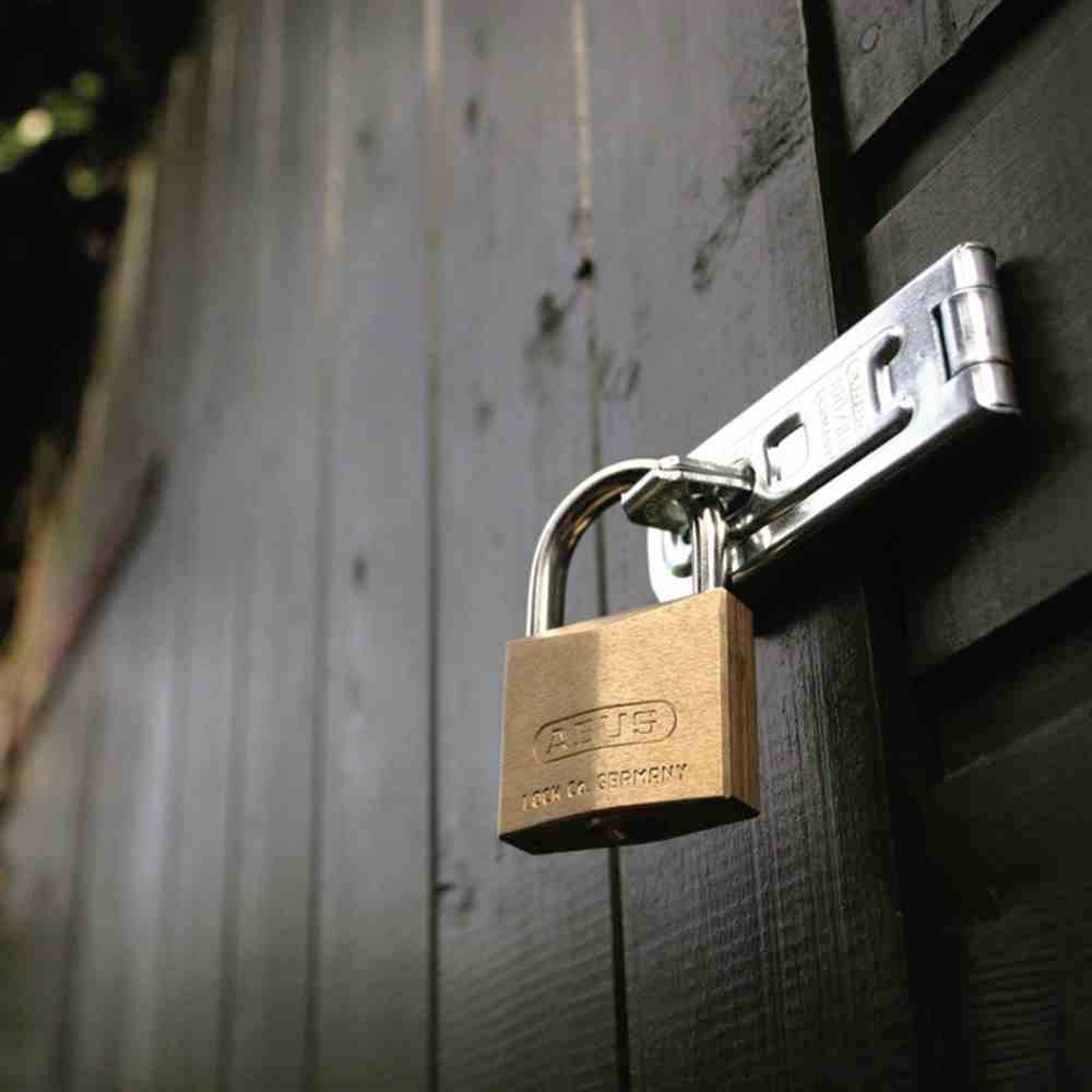 Kłódka zabezpiecza bramę lub drzwi wykonane z ciemnego drewna. Zamek jest nowy i lśniący, co symbolizuje bezpieczeństwo.