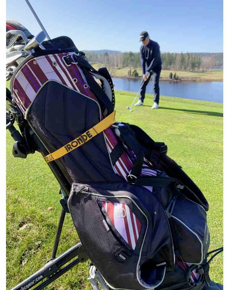 Golfista stoi na trawniku i przygotowuje się do uderzenia na putting green. Na pierwszym planie widoczna jest torba golfowa z kijami.