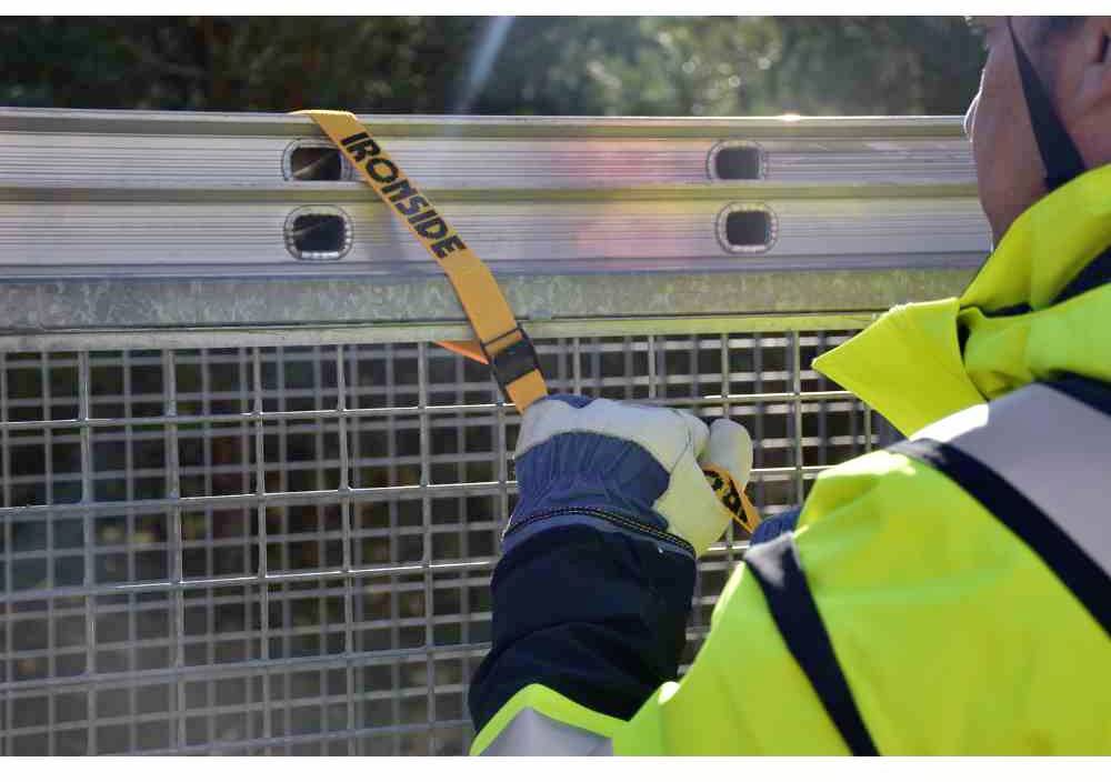 Osoba w odzieży roboczej mocuje żółty pas napinający do metalowej kratownicy.