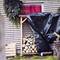 Stos drewna obok drewnianej skrzyni z gałązkami świerkowymi i przykrytą plandeką przed budynkiem z czerwoną zasłoną.