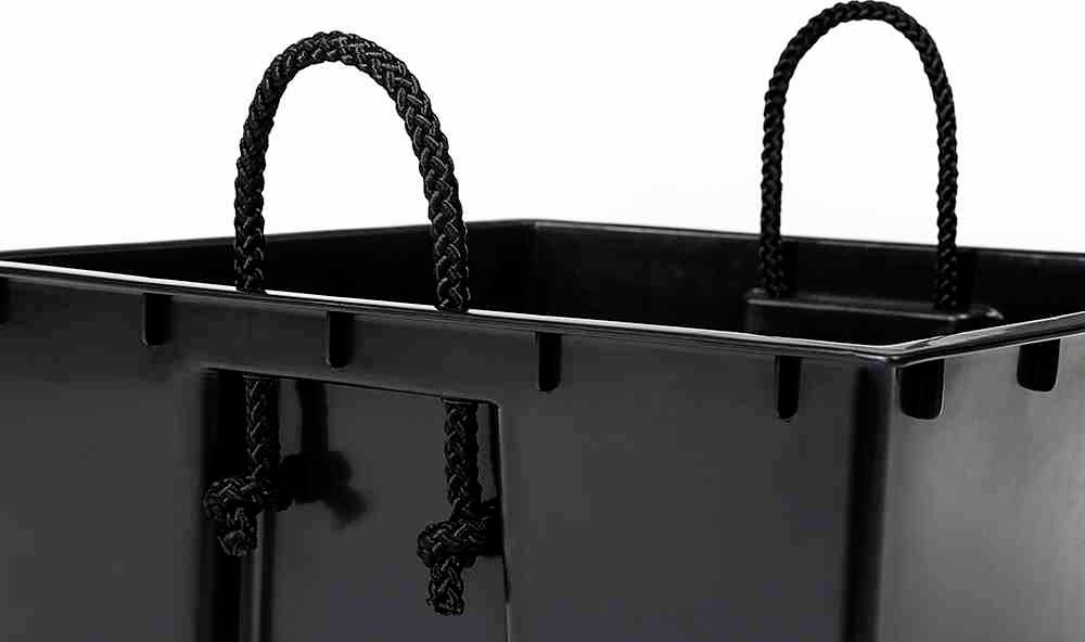 Czarny plastikowy pojemnik z dwoma plecionymi uchwytami u góry. Pojemnik posiada prostokątne wgłębienia i połyskliwą powierzchnię.