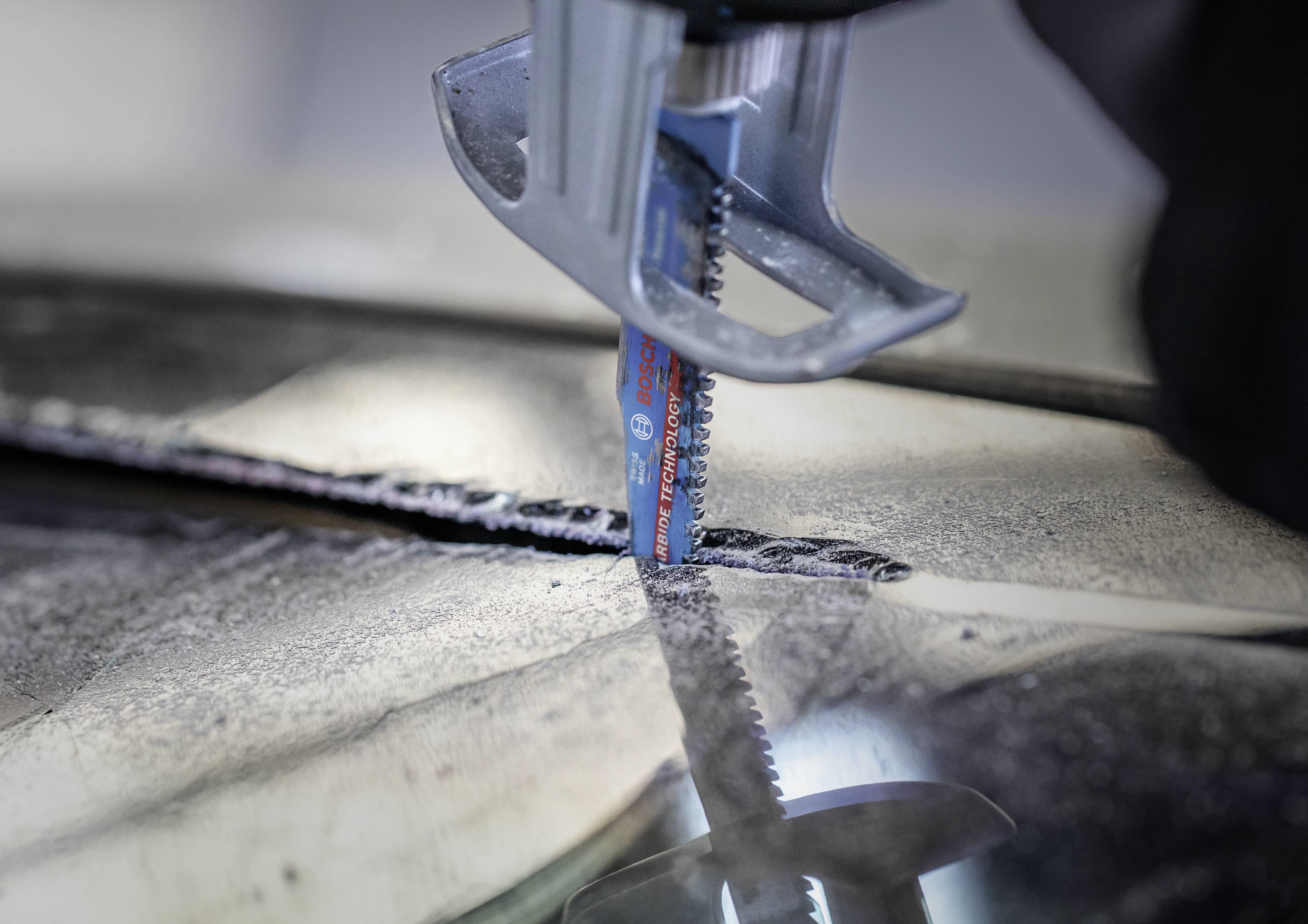 Piła metalowa przecina arkusz metalu. Ostrze piły porusza się pionowo. Widoczne są wióry i pył metalowy.