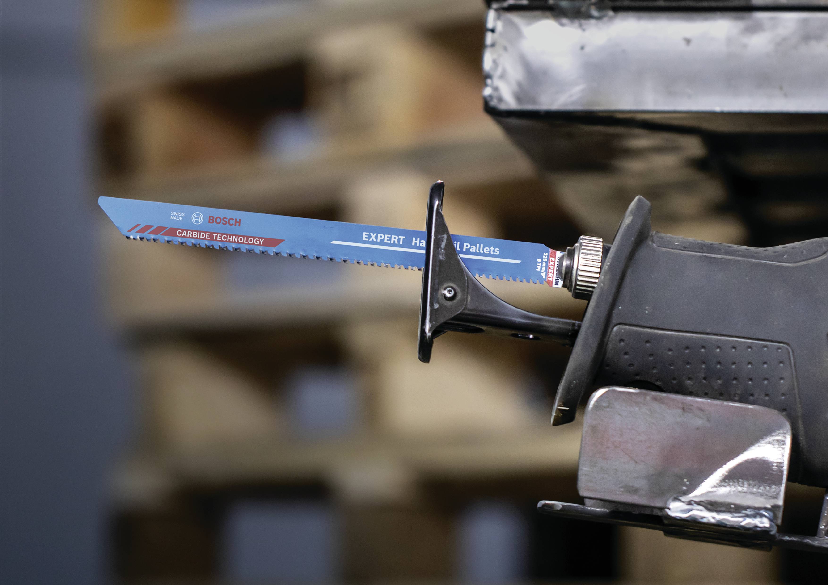 Elektryczna piła ogonowa z niebieskim brzeszczotem, w tle ułożone palety.