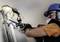 Robotnik w kasku ochronnym i masce naprawia rury w ścianie, używając piły do usunięcia uszkodzonych fragmentów.