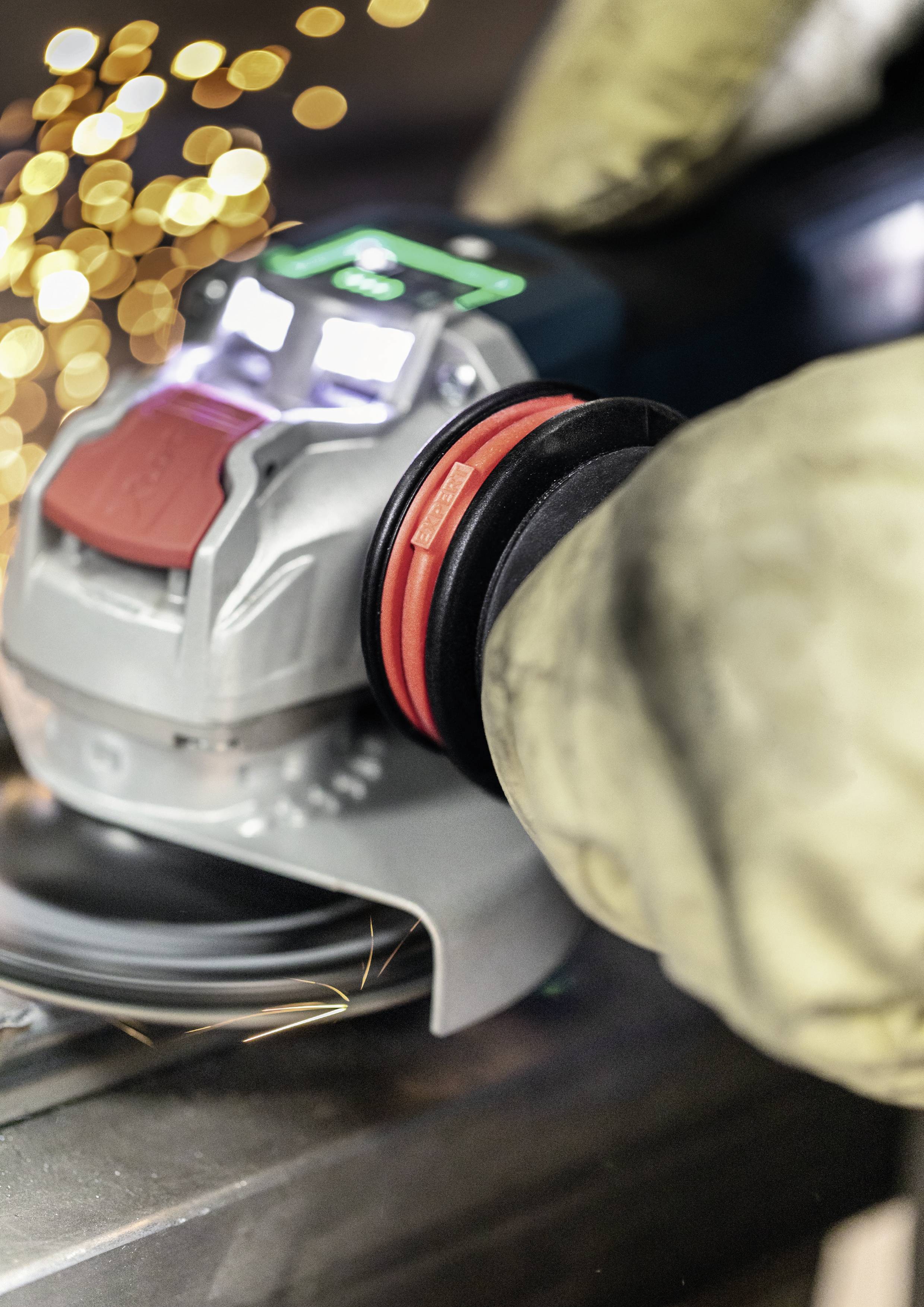 Dłoń prowadząca szlifierkę kątową, z lecącymi iskrami w tle. Osoba jest w ochronnych rękawicach.