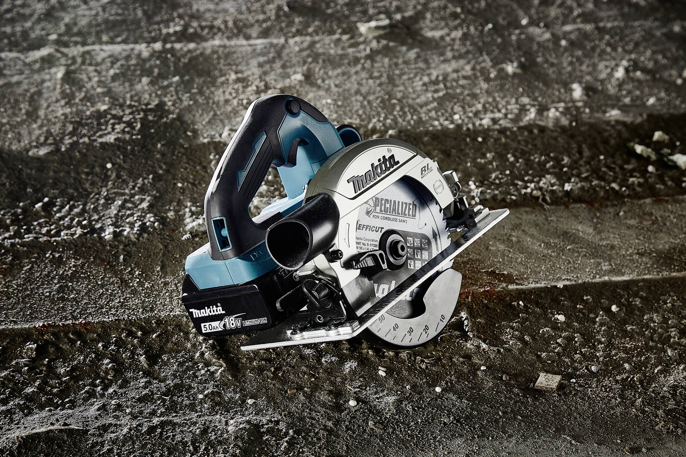 Ręczna piła tarczowa leży ukośnie na betonowej podłodze. Piła ma obudowę w kolorze niebiesko-czarnym i widoczną tarczę tnącą.