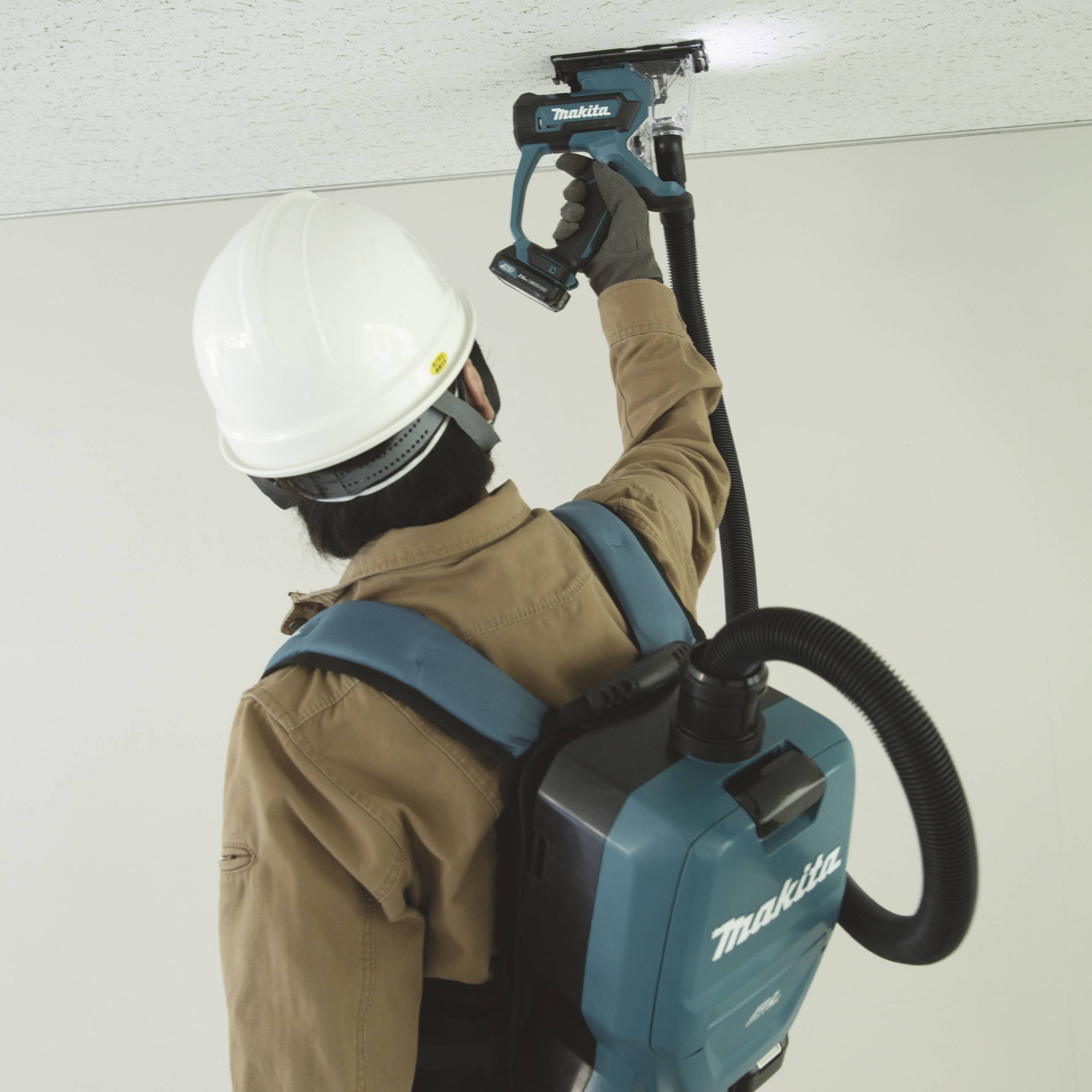 Osoba ubrana w odzież ochronną używa przenośnego narzędzia malarskiego na suficie, aby nanieść lub usunąć farbę.