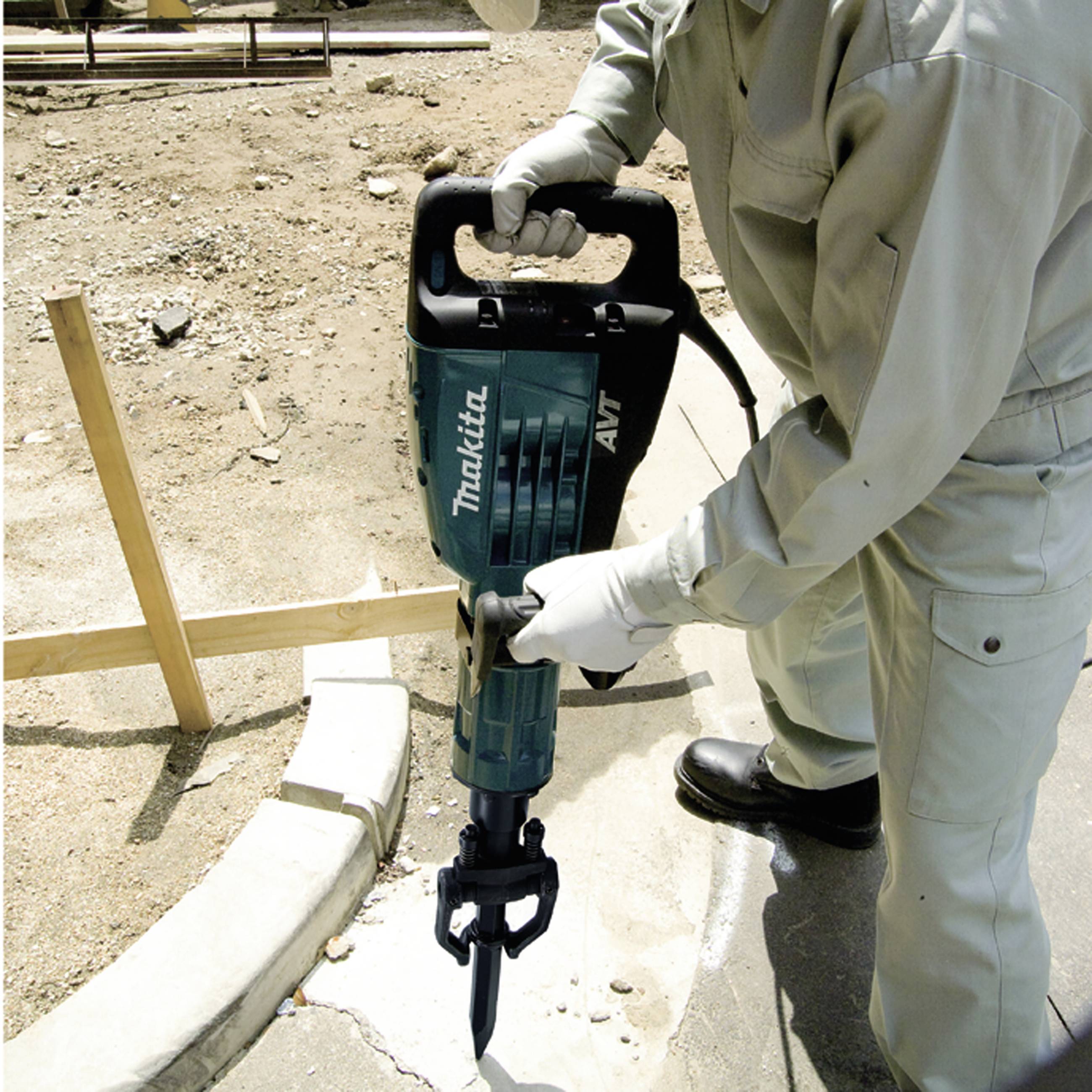 Osoba używa młota elektrycznego na placu budowy. Nosi odzież ochronną i pracuje na powierzchni betonowej.