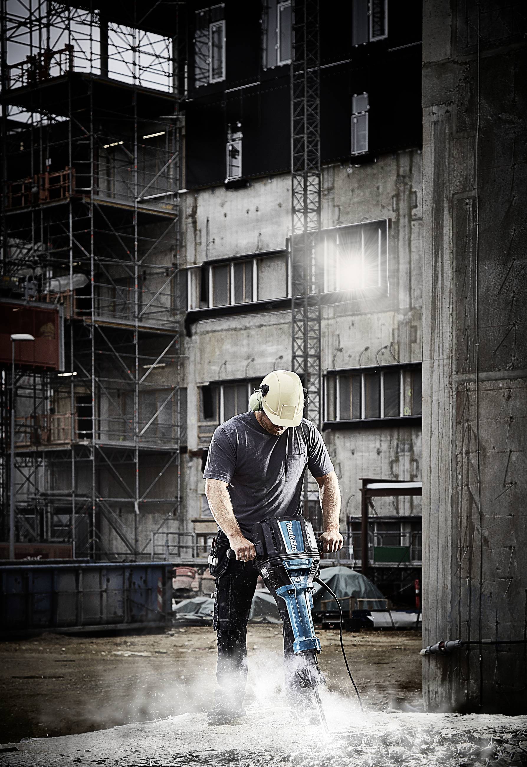 Osoba pracuje na budowie za pomocą młota pneumatycznego. W tle widoczne są rusztowania i budynki.