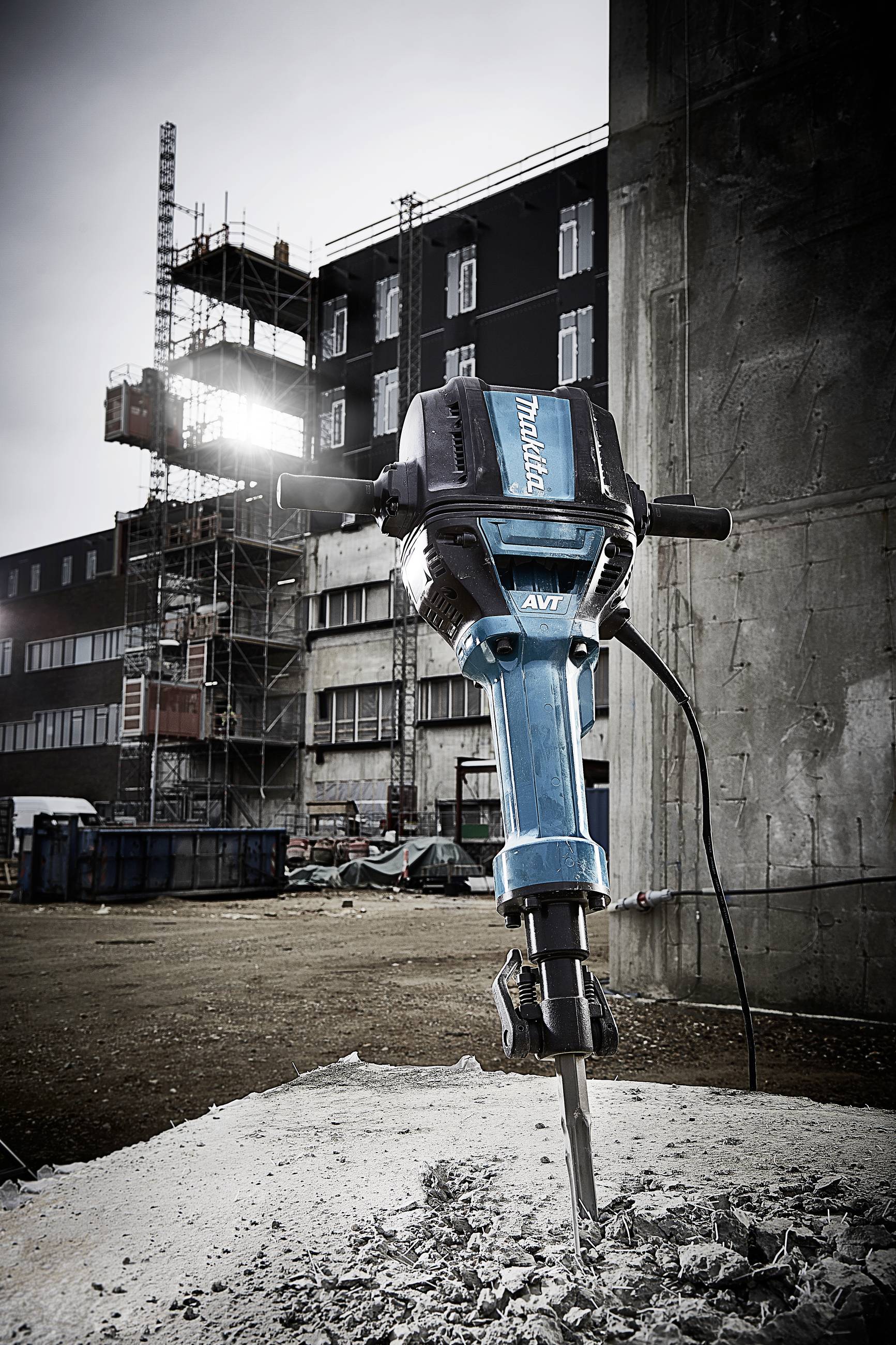 Pneumatyczny młot uderzeniowy w trakcie pracy na placu budowy. W tle widoczny jest budynek w trakcie budowy oraz rusztowania.