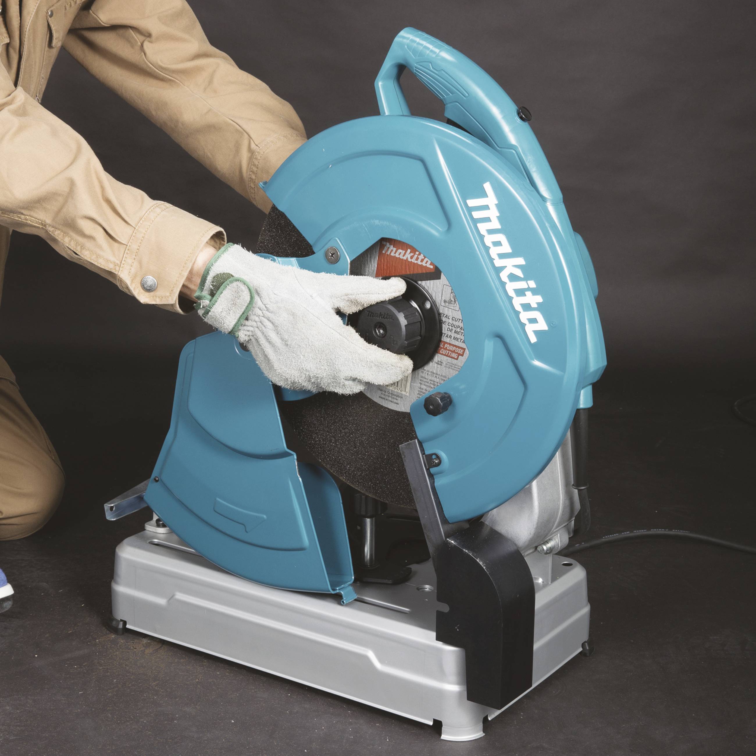 Osoba ubrana w strój roboczy używa niebieskiej maszyny tnącej do cięcia metalu. Osoba ta nosi rękawice ochronne.